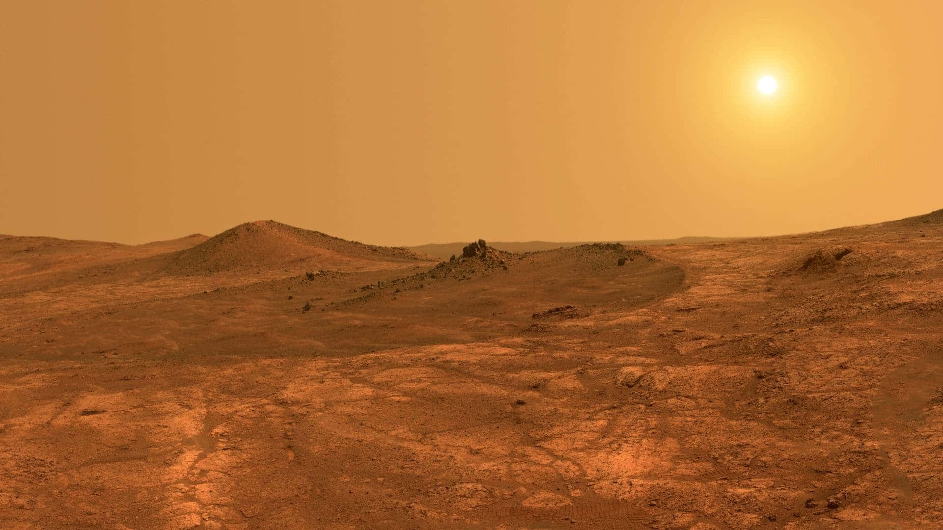 火星表面的異域風景 壁紙 — 廣闊的鏽紅色火星景觀沐浴在金色陽光下，起伏的沙丘和遠處的岩石露頭在朦朧的橙色天空下。