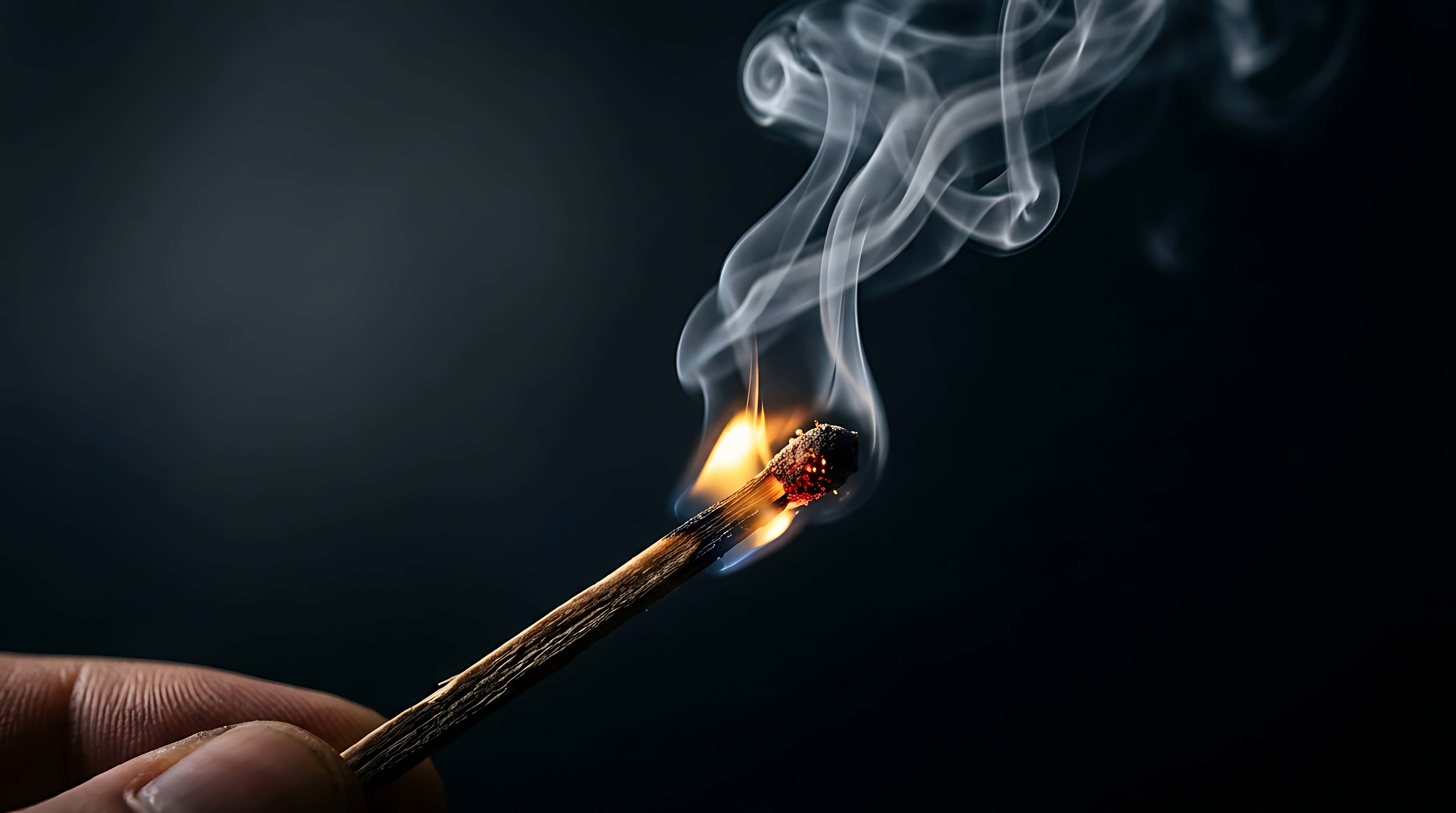 火柴點燃時的火焰與動態煙霧旋渦，電影感火源特寫 壁紙 — 一隻手拿著一根點燃的火柴，在黑暗背景下投射出溫暖的光和捲曲的煙霧。
