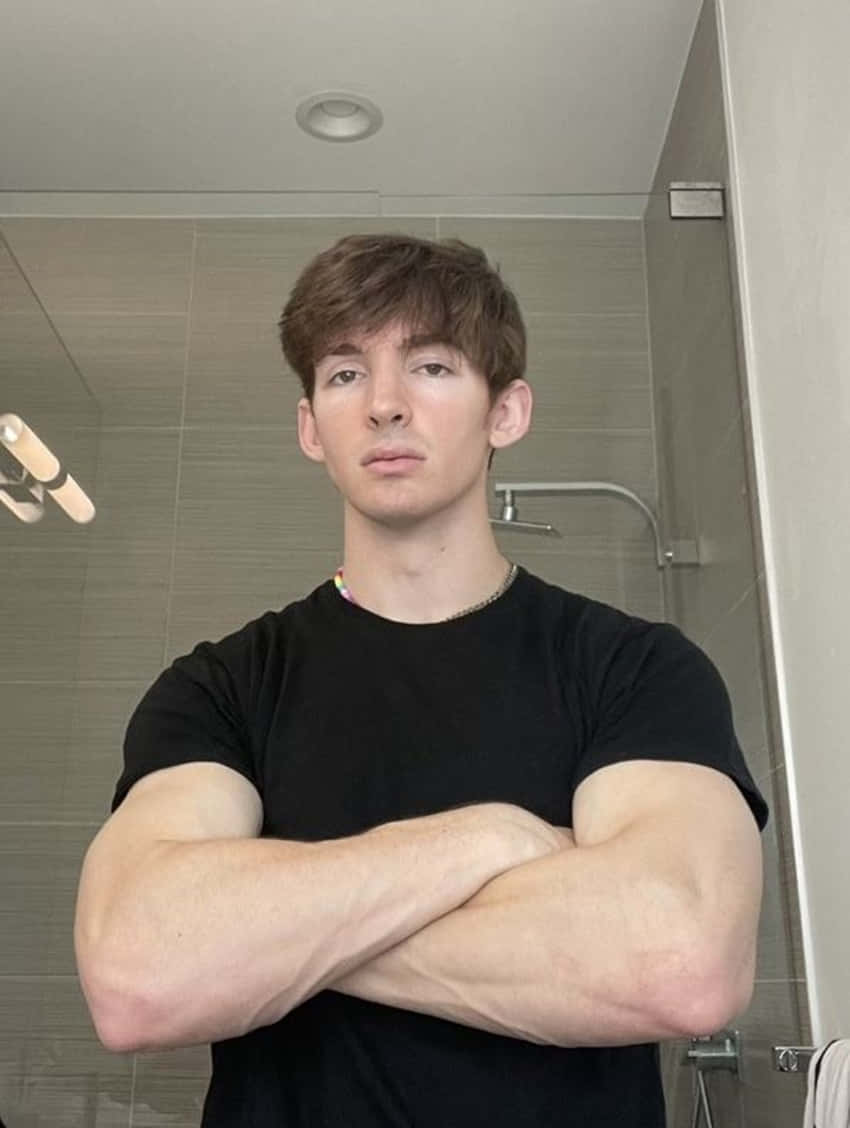 年輕肌肉男站在浴室中雙臂交叉身穿黑色T恤。