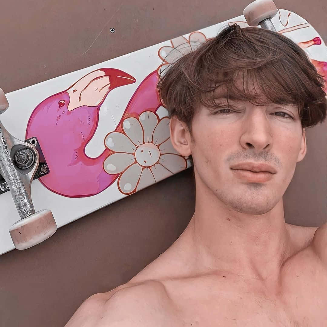 年輕男子將頭靠在帶有火烈鳥和雛菊圖案的滑板上。