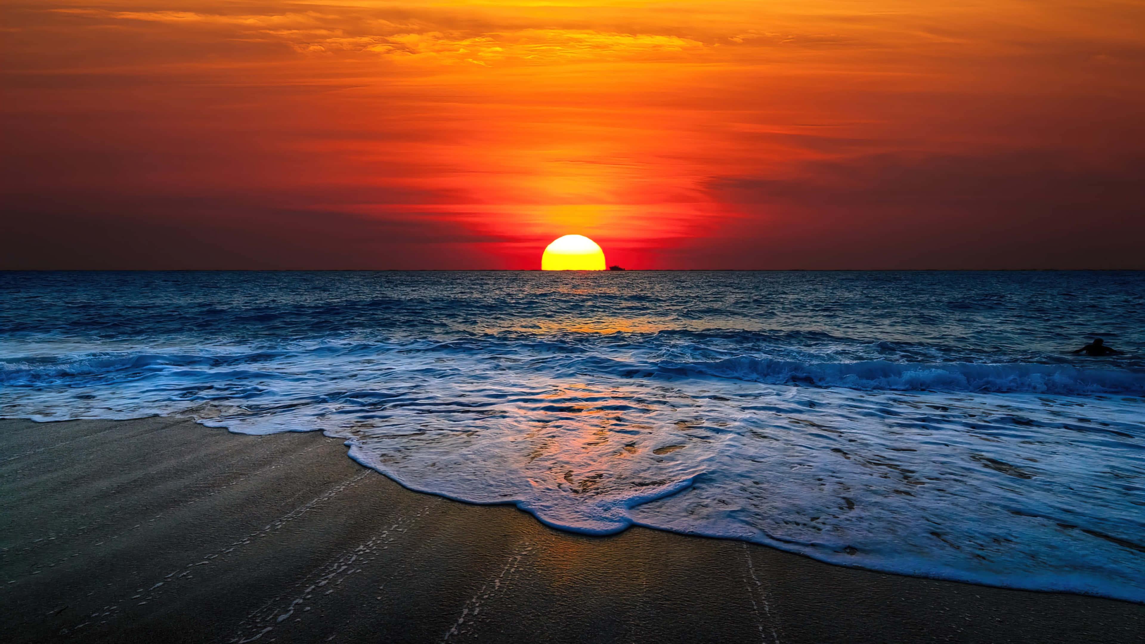 Sunset Wave 桌布 壁紙 — 火熱的橙色夕陽在平靜的海洋上落下，海浪輕輕拍打著沙灘。