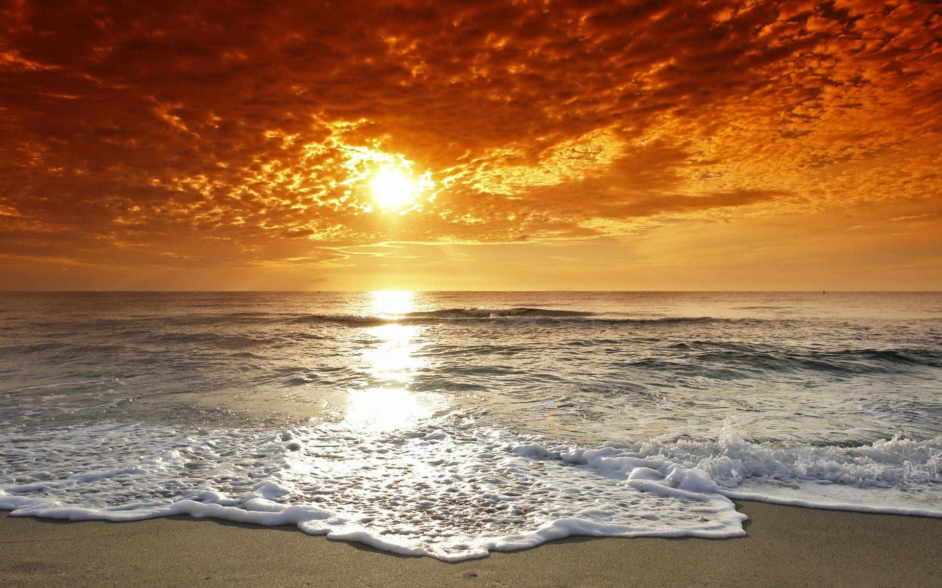 海灘日落 桌布 壁紙 — 火熱的橙色日落染紅了平靜海洋上的天空，海浪輕輕拍打沙灘。