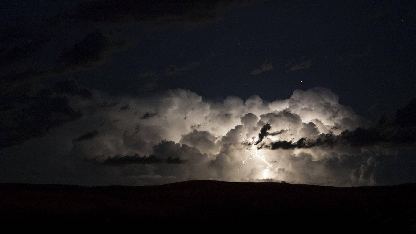 閃電在夜間穿過暴風雲，照亮黑暗的山丘。