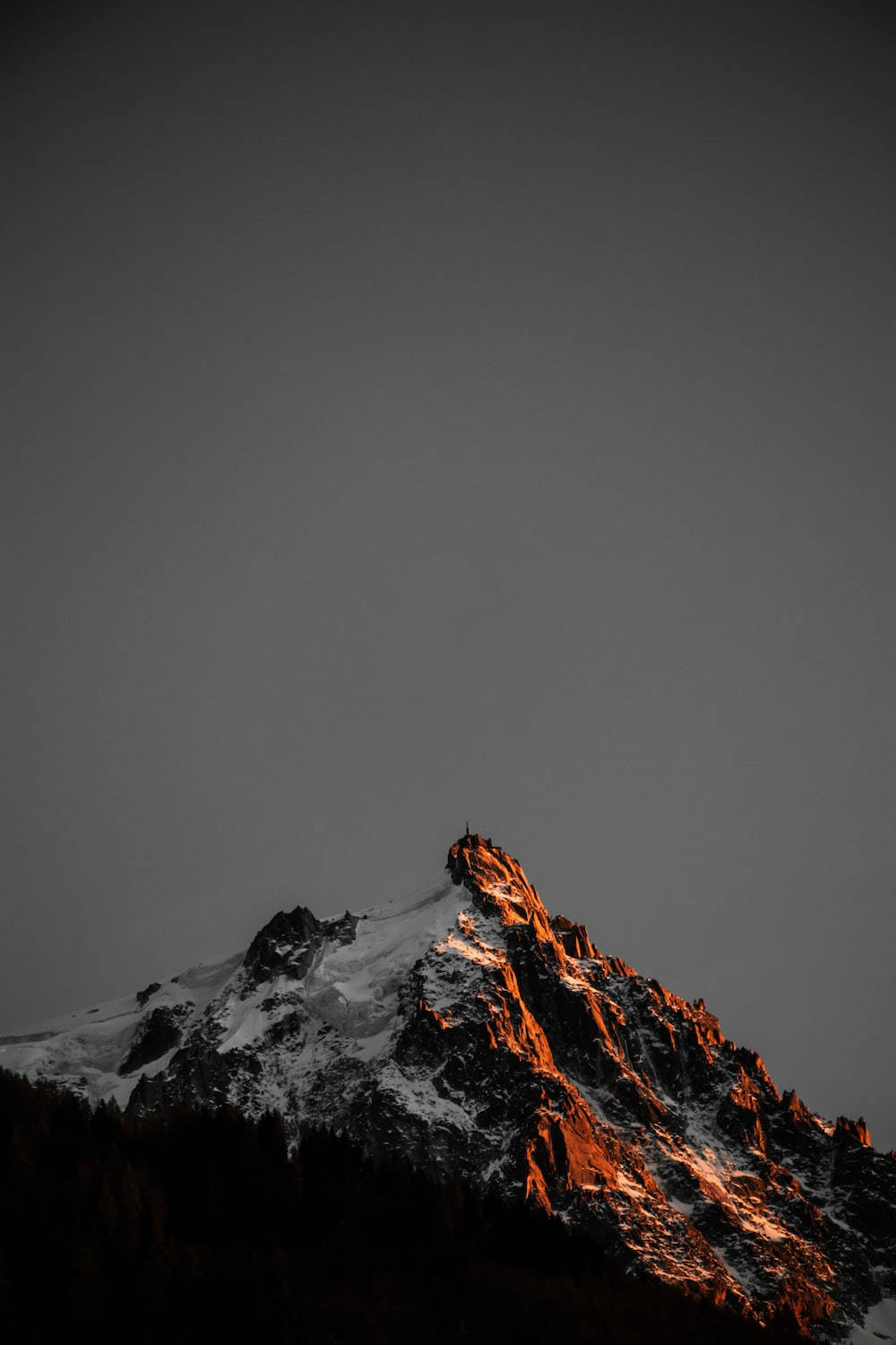 灰棕山巒手機壁紙 壁紙 — 黃昏時分，白雪覆蓋的山峰沐浴在溫暖的金色光芒中，映襯著深灰色的天空。