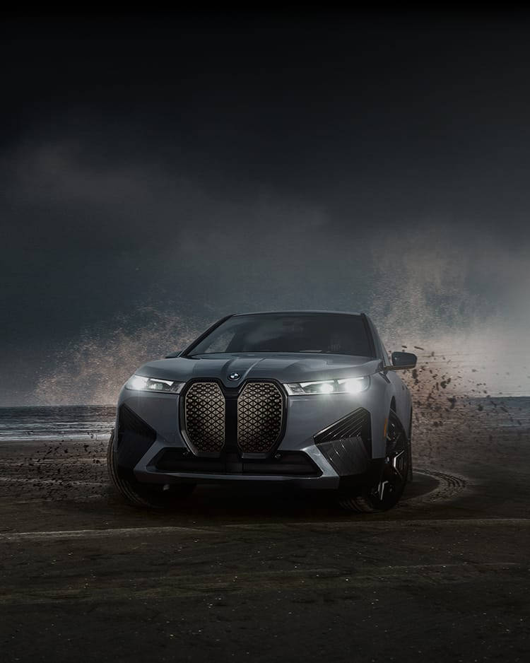 銀色BMW SUV在暴風雨夜晚的海灘沙地上行駛。