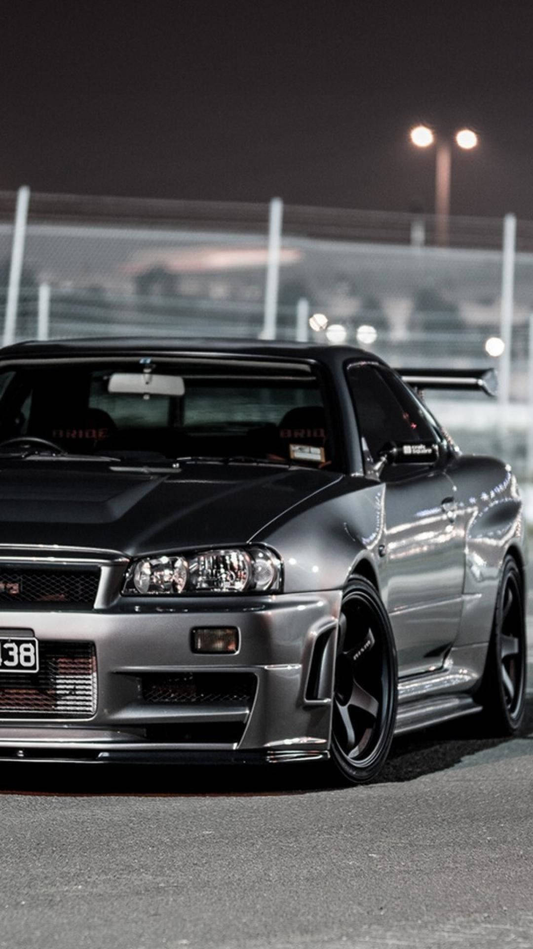銀色日產Skyline GT-R在夜間停泊在賽車場上，明亮燈光下。