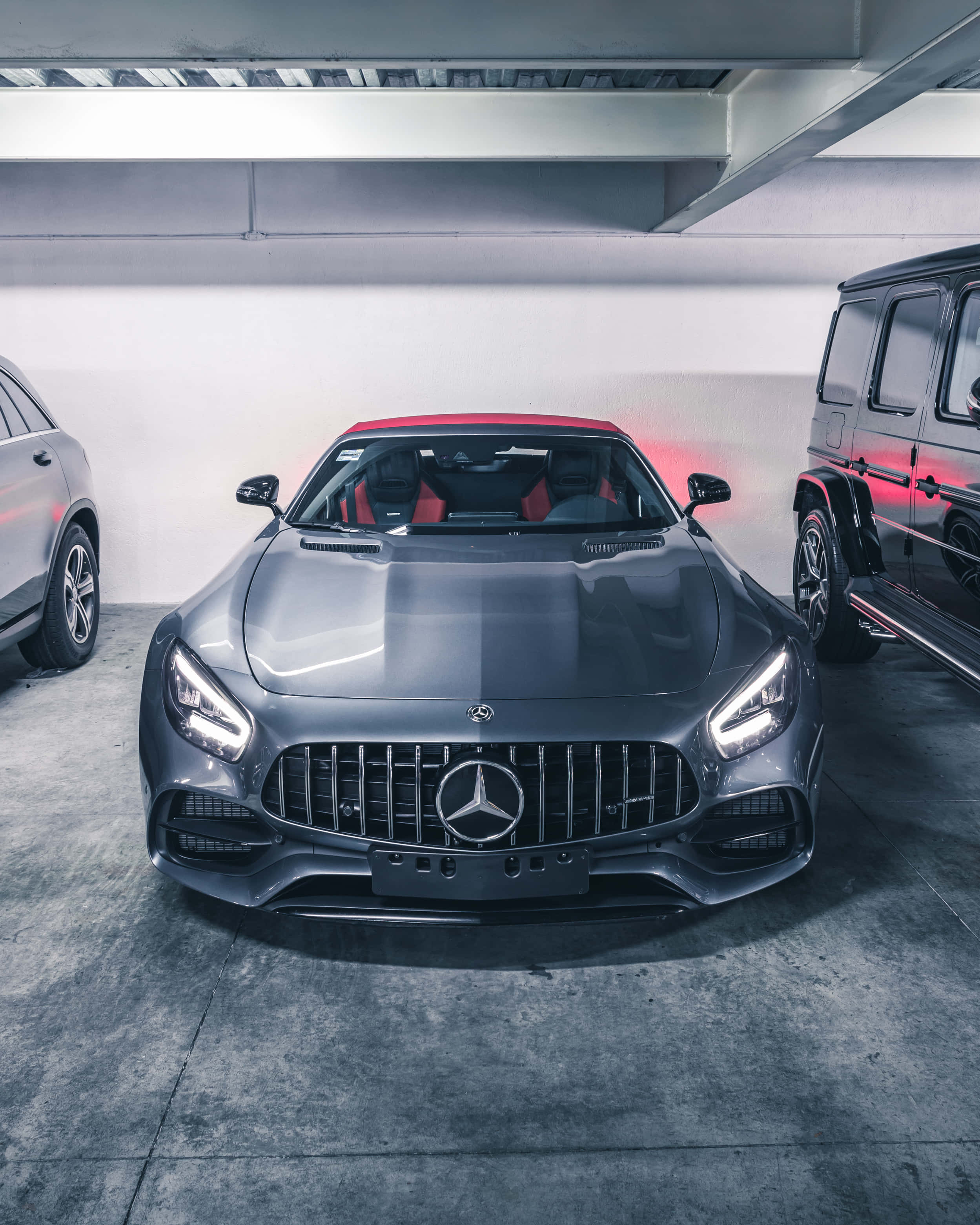 灰色AMG GT-R停車場背景壁紙 壁紙 — 一輛時尚的灰色Mercedes-AMG GT帶有紅色點綴，在涼爽的車庫燈光下與其他豪華車輛並排閃耀。