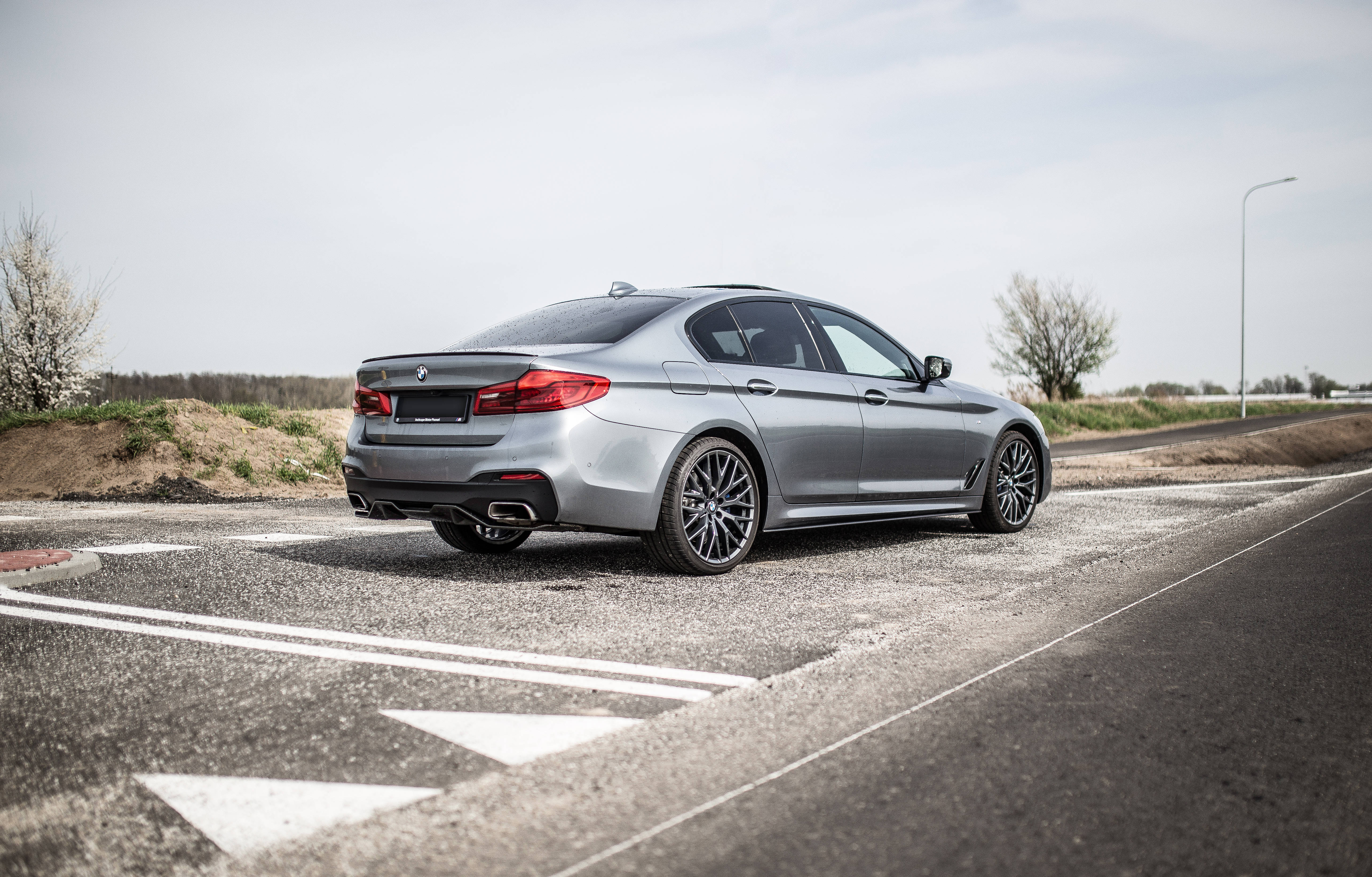 灰色BMW M5系列 壁紙 — 一架時尚的銀色寶馬轎車停在有白色標記的瀝青路上，天空多雲。