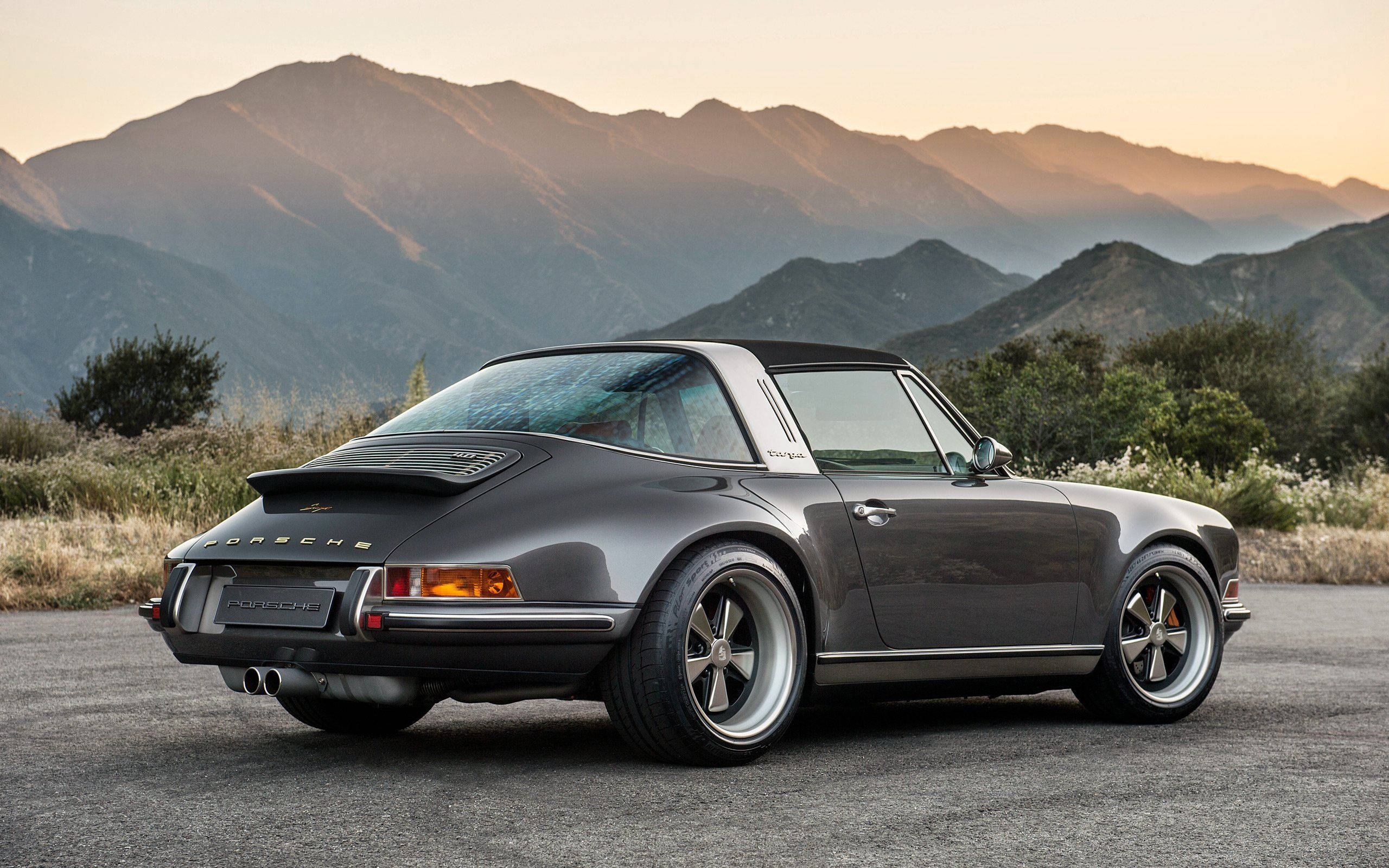 灰色Singer保時捷後視 壁紙 — 一架流線型灰色保時捷911 Targa停泊在瀝青路上，背後是沐浴在金色夕陽餘暉中的山脈。