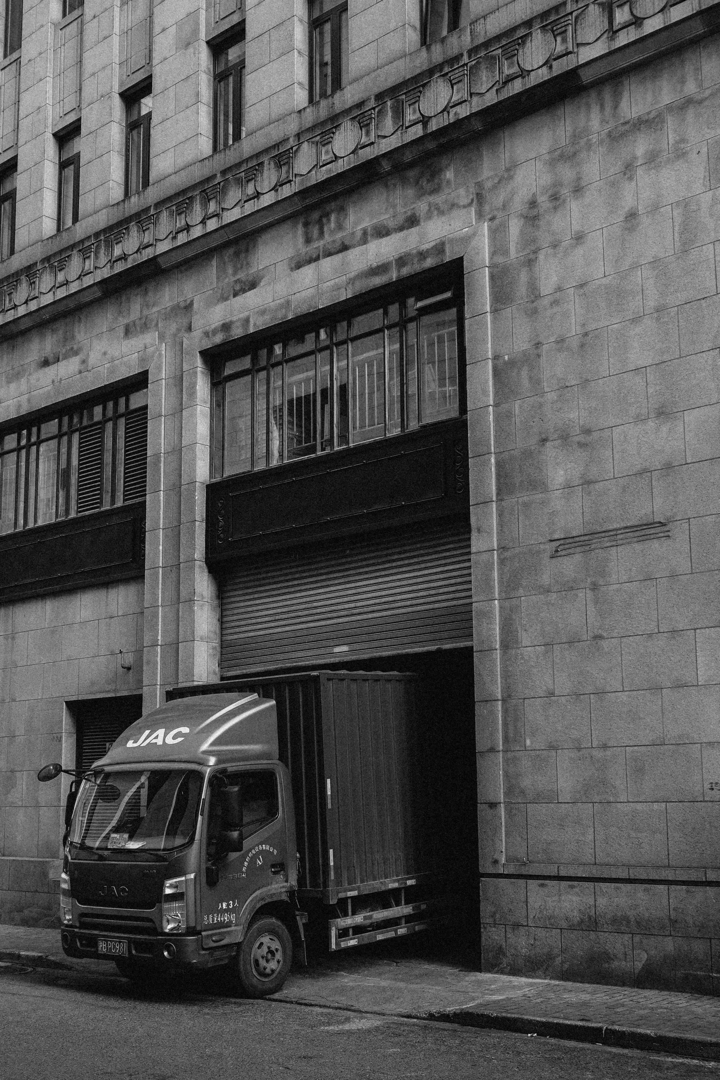 灰色江淮卡車車輛 壁紙 — 一輛江淮卡車停在一個風化石建築的裝卸碼頭旁的黑白照片，建築帶有華麗的建築細節。