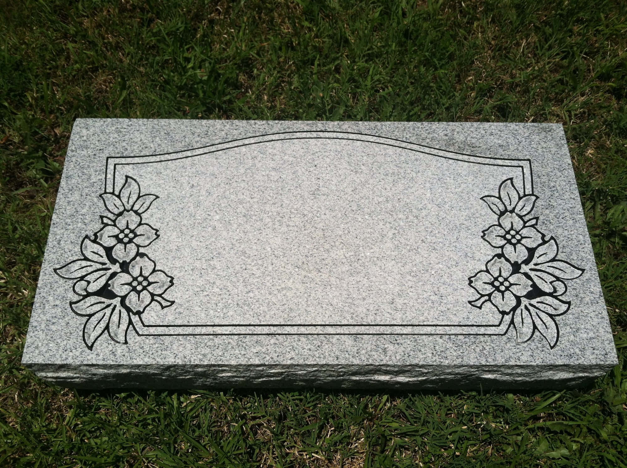 Gravestone 桌布 壁紙 — 灰色花崗岩墓碑上刻有花卉圖案，在日光下放置在綠色草地上。