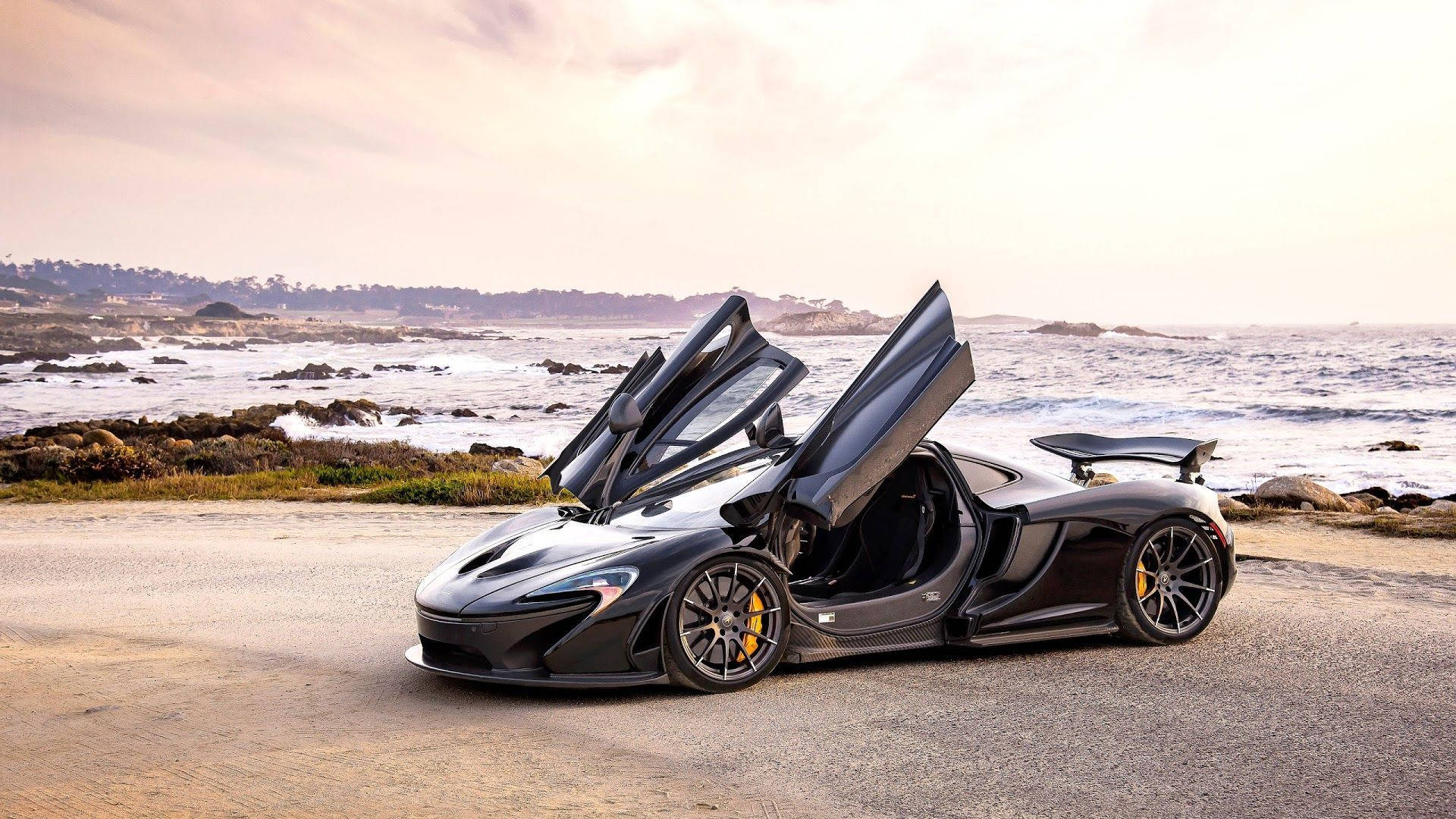 灰色麥拉倫P1 壁紙 — 一架時尚的黑色McLaren跑車，蝴蝶門打開，停在日落時分的海岸公路上。