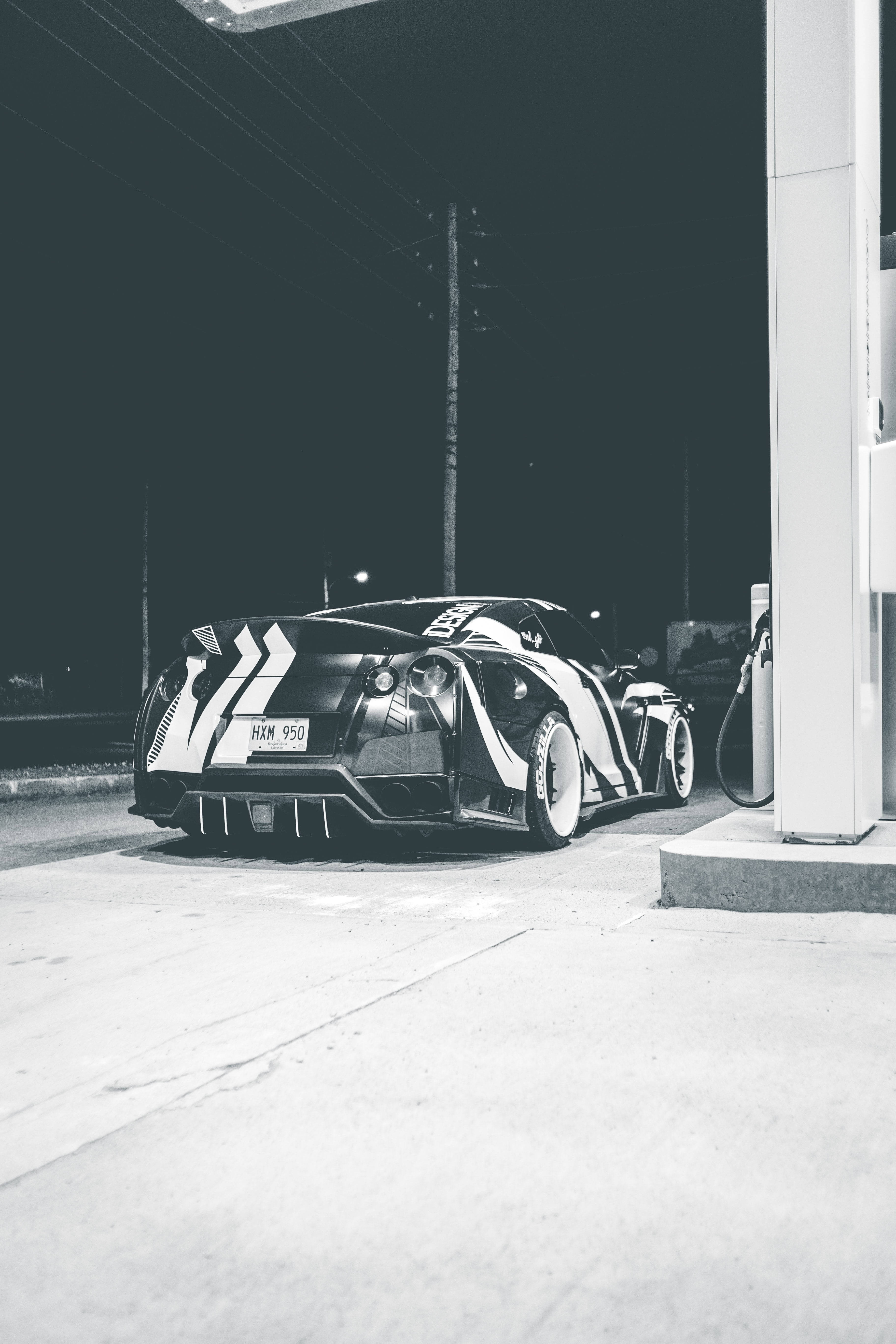 灰階加油站 壁紙 — 一輛時尚的黑白定制跑車在夜間停在加油站，燈光效果戲劇化。