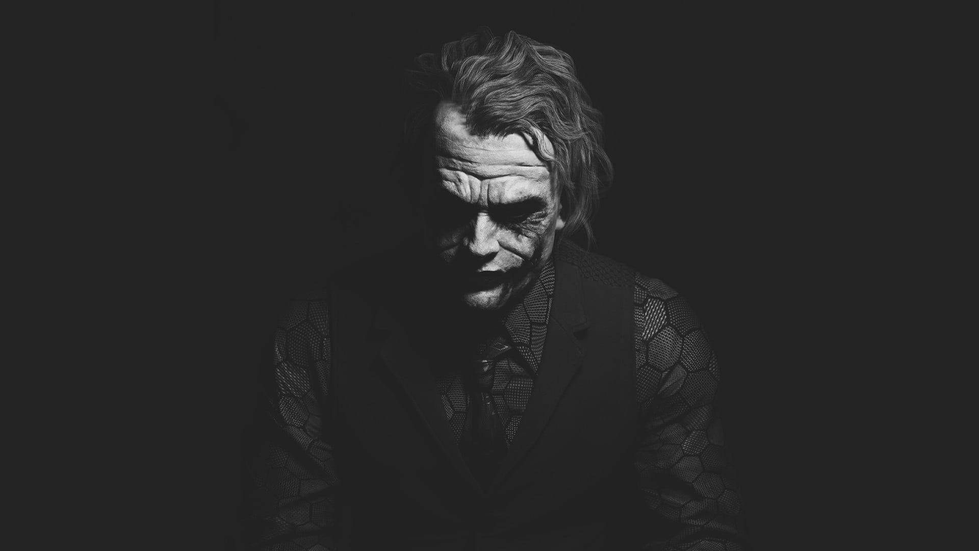 一個帶有塗抹白色臉部化妝和深色西裝的威脅性小丑，在黑色背景下強烈凝視。