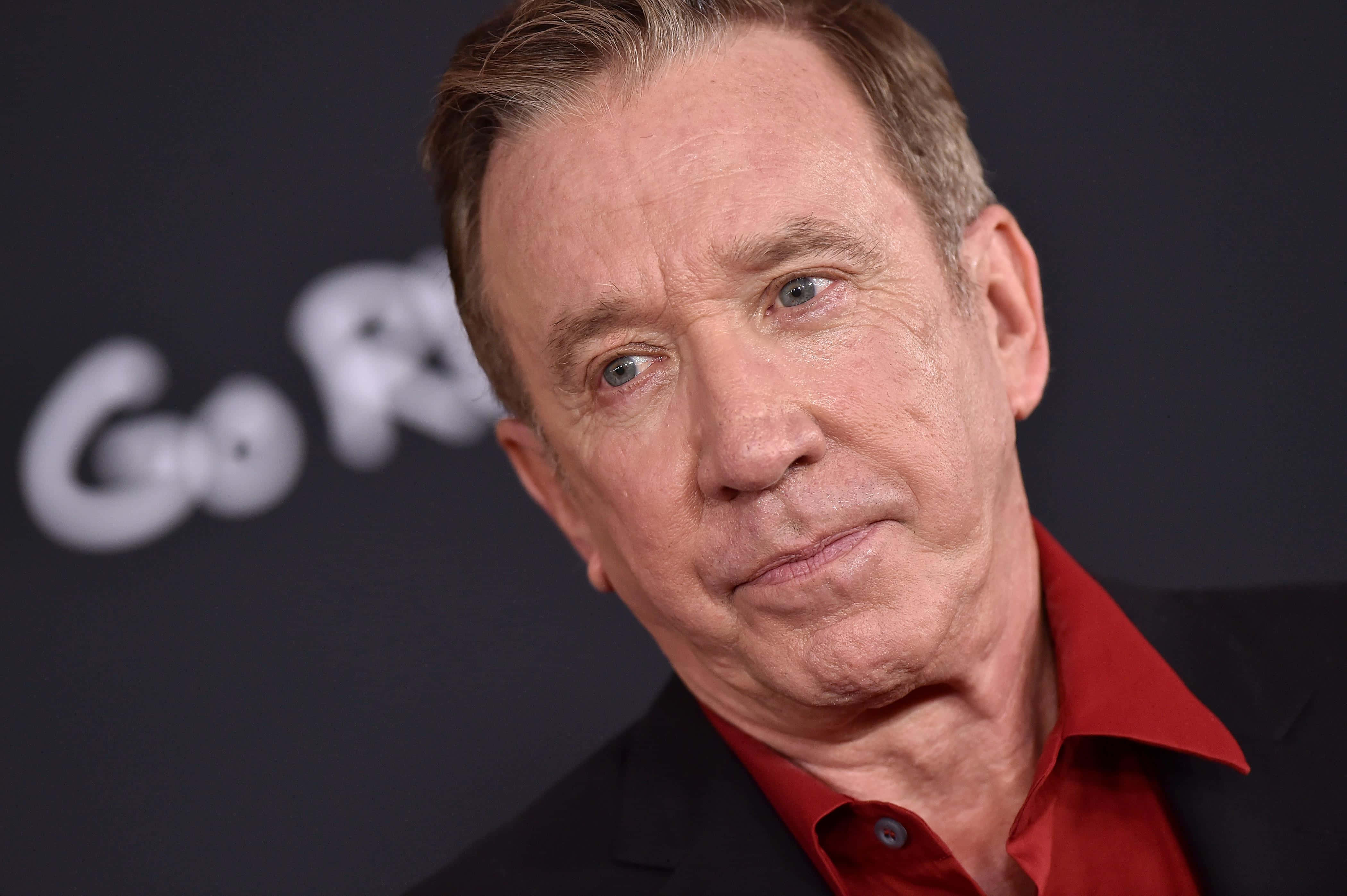Tim Allen 桌布 壁紙 — 灰髮藍眼男士穿著紅色襯衫和黑色西裝外套，在深色背景上有模糊白色文字的近距離肖像。