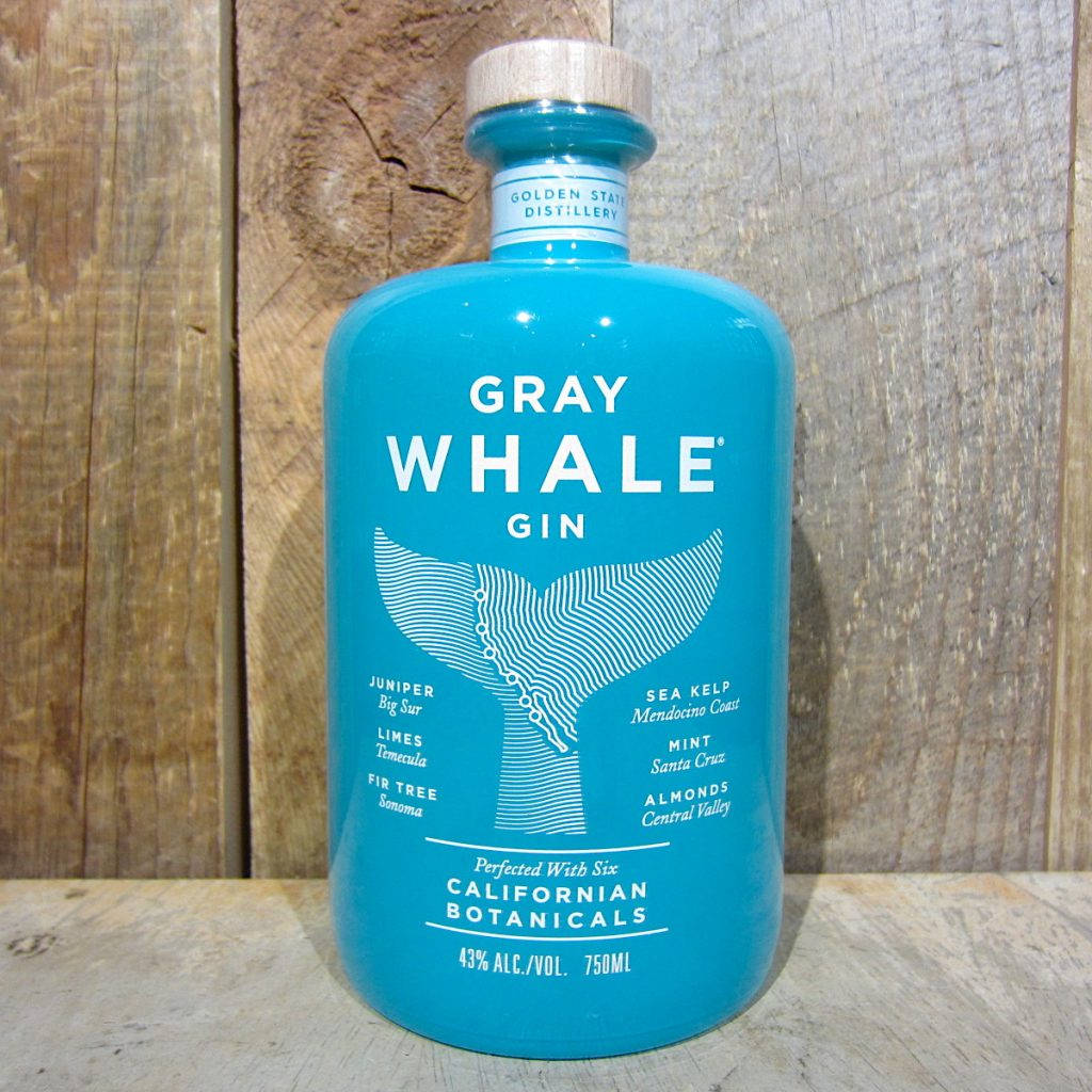 灰鯨金酒瓶置於木質背景前 壁紙 — 一個充滿活力的藍綠色Gray Whale Gin酒瓶，帶有鯨魚尾巴設計，放在質樸的木頭上，背景是風化的木質背景。