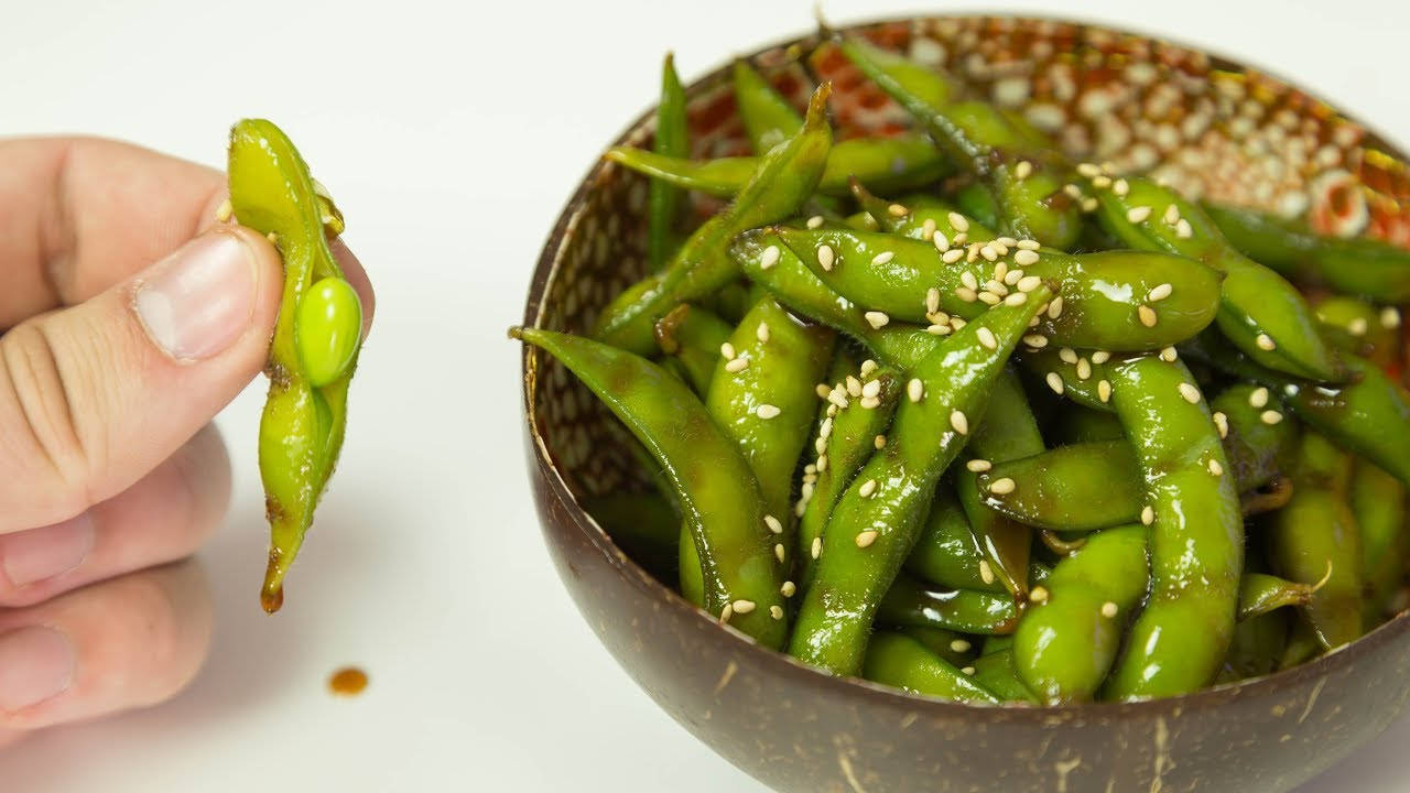 手拿毛豆莢放在芝麻毛豆碗上方。