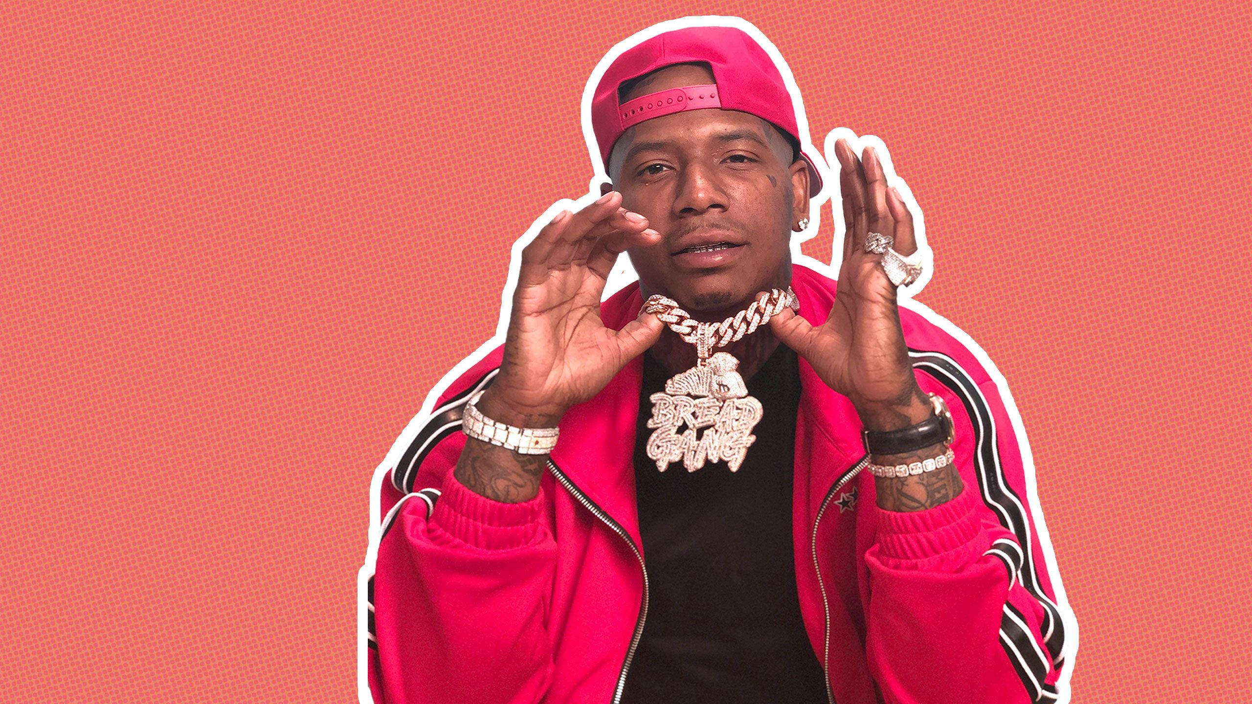 炫目 Moneybagg Yo 壁紙 — 一名身穿亮粉紅色外套和帽子的男子，在帶有紋理的珊瑚色背景前，佩戴閃亮珠寶自信地擺姿勢。