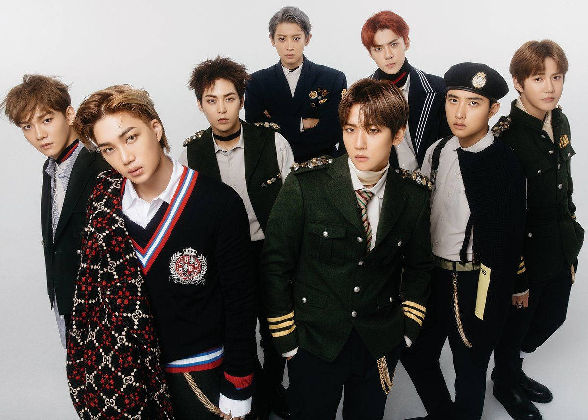 七位男性K-pop偶像穿著正式的軍事風格服裝，為攝影棚照片擺姿勢。
