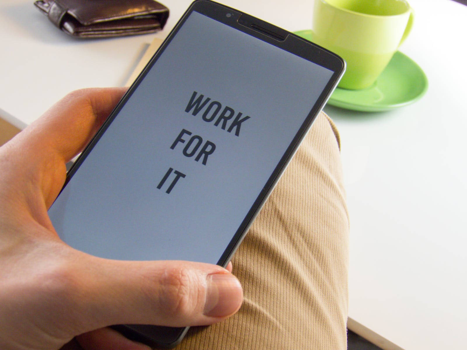 手拿著手機，旁邊有咖啡杯和錢包，顯示 'WORK FOR IT' 訊息。