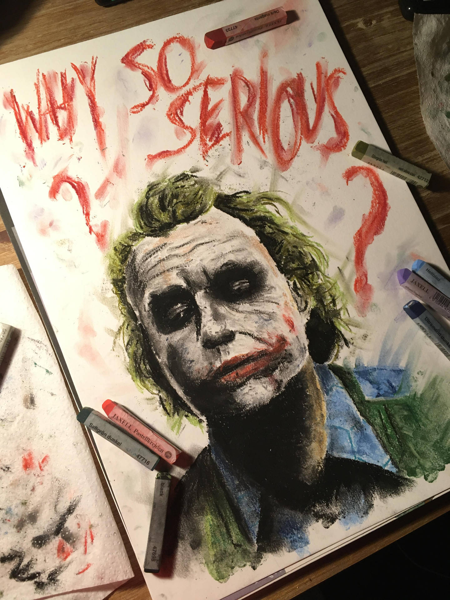 手繪小丑肖像，帶有「WHY SO SERIOUS?」文字和木質表面上的美術用品。