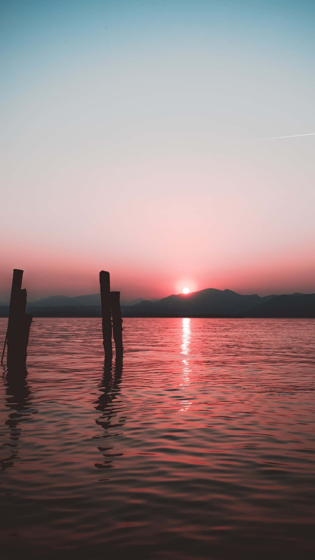 夕陽下水中兩根柱子，背景有山