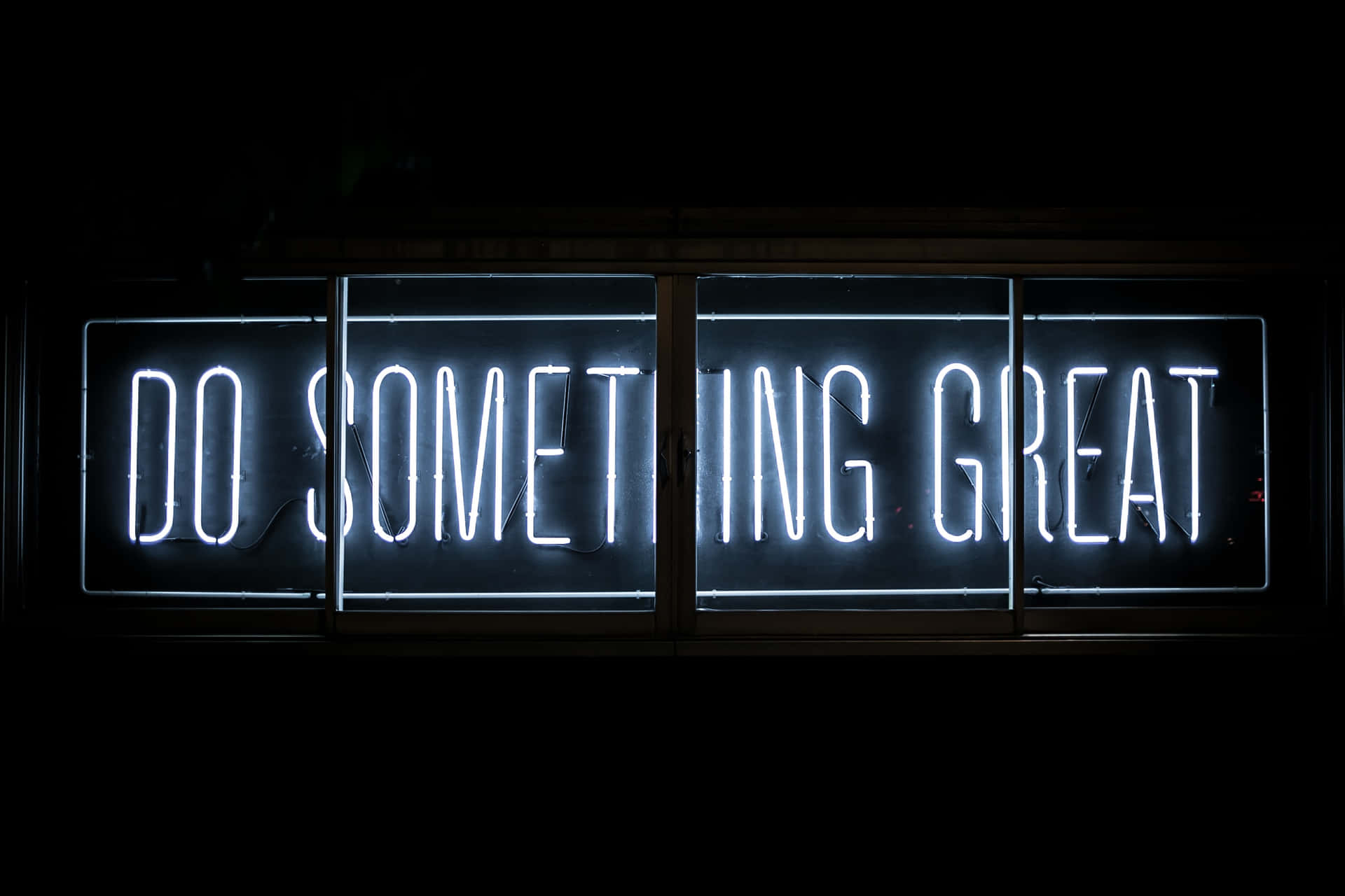 一個明亮的白色霓虹燈牌，在黑暗中寫著「DO SOMETHING GREAT」。