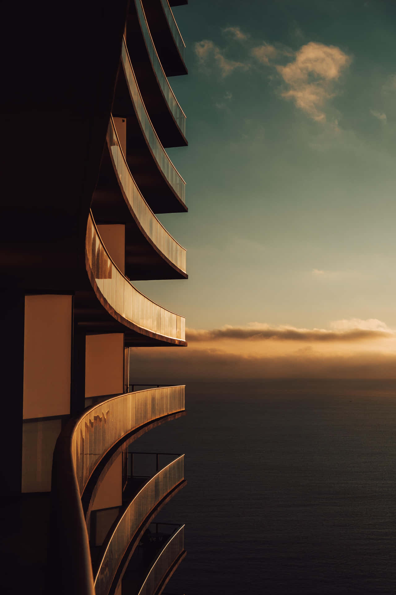 沐浴在金色日落光芒中的現代海邊建築弧形陽台。