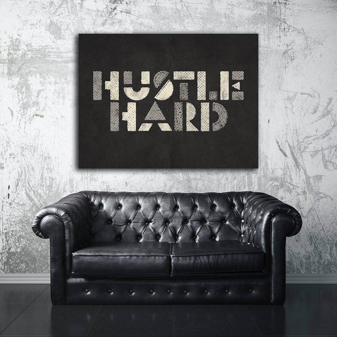 工業空間中「HUSTLE HARD」牆面藝術下的黑色皮革切斯特菲爾德沙發。