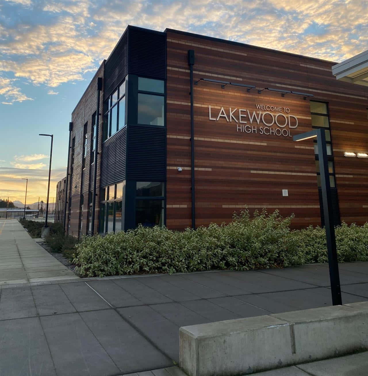 為光明未來做好準備——高中 壁紙 — 現代化的 Lakewood 高中建築，採用木材和黑色鑲板，在金色夕陽天空下。