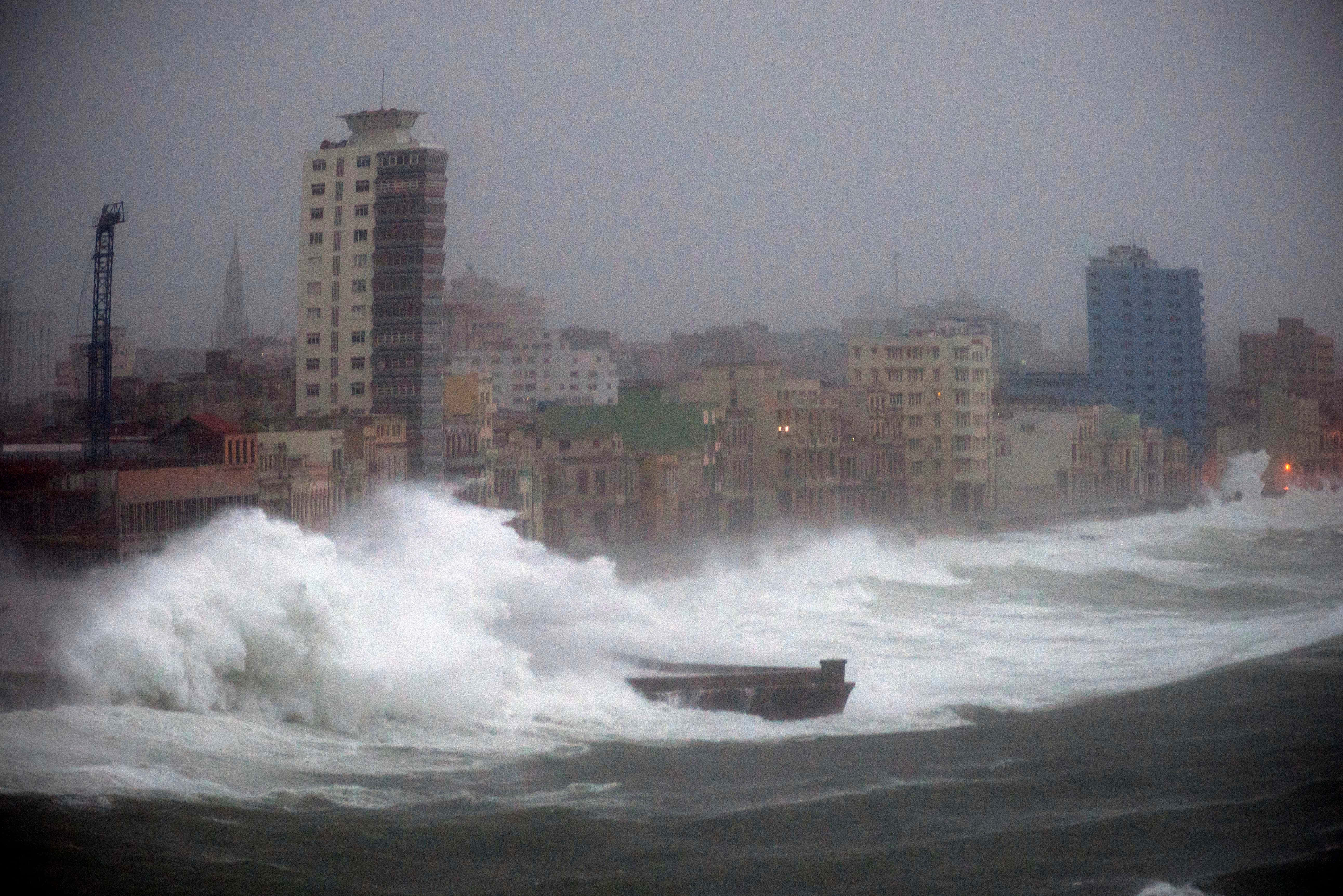 為可能的颶風做準備 壁紙 — 巨大的破碎海浪吞噬了暴風雨灰色天空下的沿海城市景觀，建築物在薄霧中幾乎看不見。