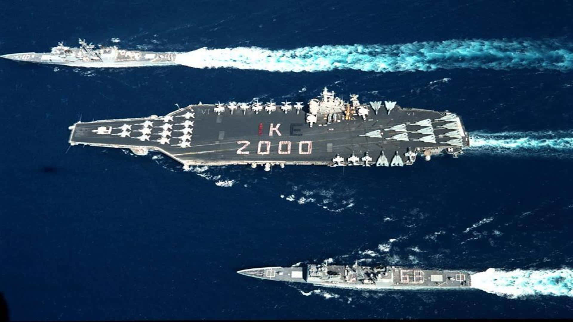 為國家英勇服役 壁紙 — 航空母艦IKE 2000在兩艘驅逐艦護航下，劃破深藍色海洋的鳥瞰圖。