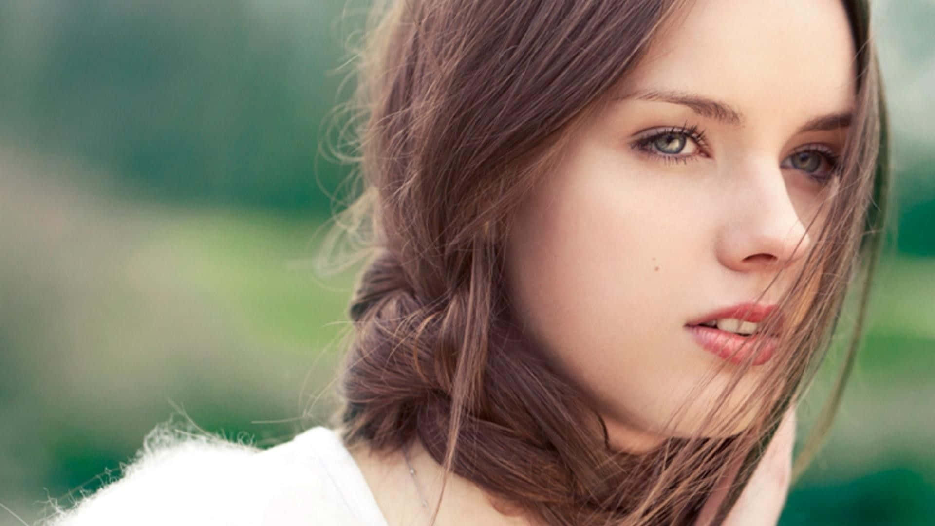 為女孩之美設計的高質感壁紙 壁紙 — 一位棕色頭髮、藍色眼睛的年輕女性，在柔和的綠色模糊背景下若有所思地凝視著。
