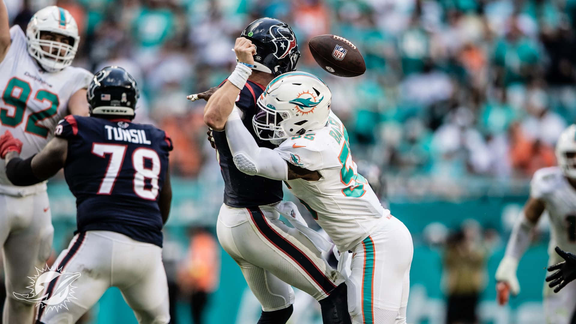為您最愛的 NFL 球隊加油助威 壁紙 — 邁阿密海豚隊的防守球員在日間NFL比賽中，在空中擒抱侯斯頓德克薩斯人隊的四分衛，同時足球在空中飛過。