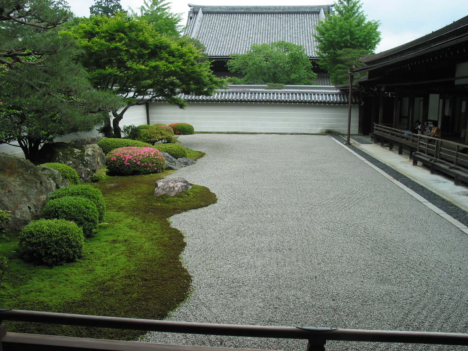 為您的車道增添趣味設計 壁紙 — 一個寧靜的日本花園，耙過的碎石小徑蜿蜒穿過長滿苔蘚的綠植和盛開的粉紅色杜鵑花，下方是傳統的木結構建築。