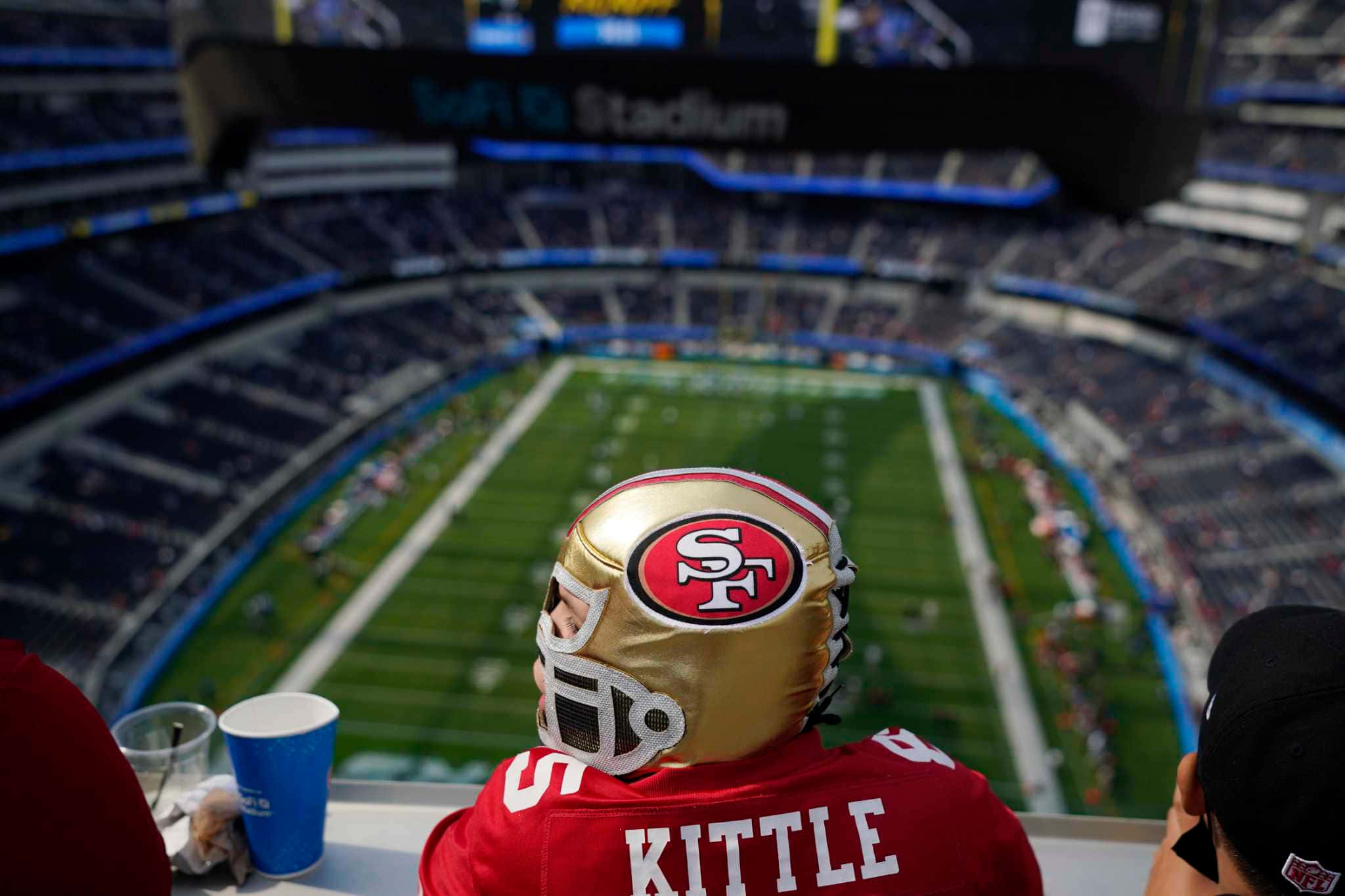 為球迷準備就緒的SoFi Stadium 壁紙 — 一位年輕球迷戴著金色頭盔和紅色球衣，在Levi's Stadium的上層看台觀看足球比賽。