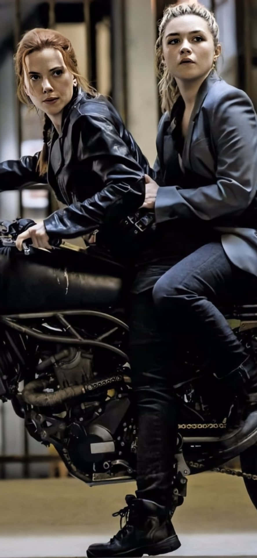 兩位身穿皮夾克和西裝的女性在工業環境中騎摩托車。