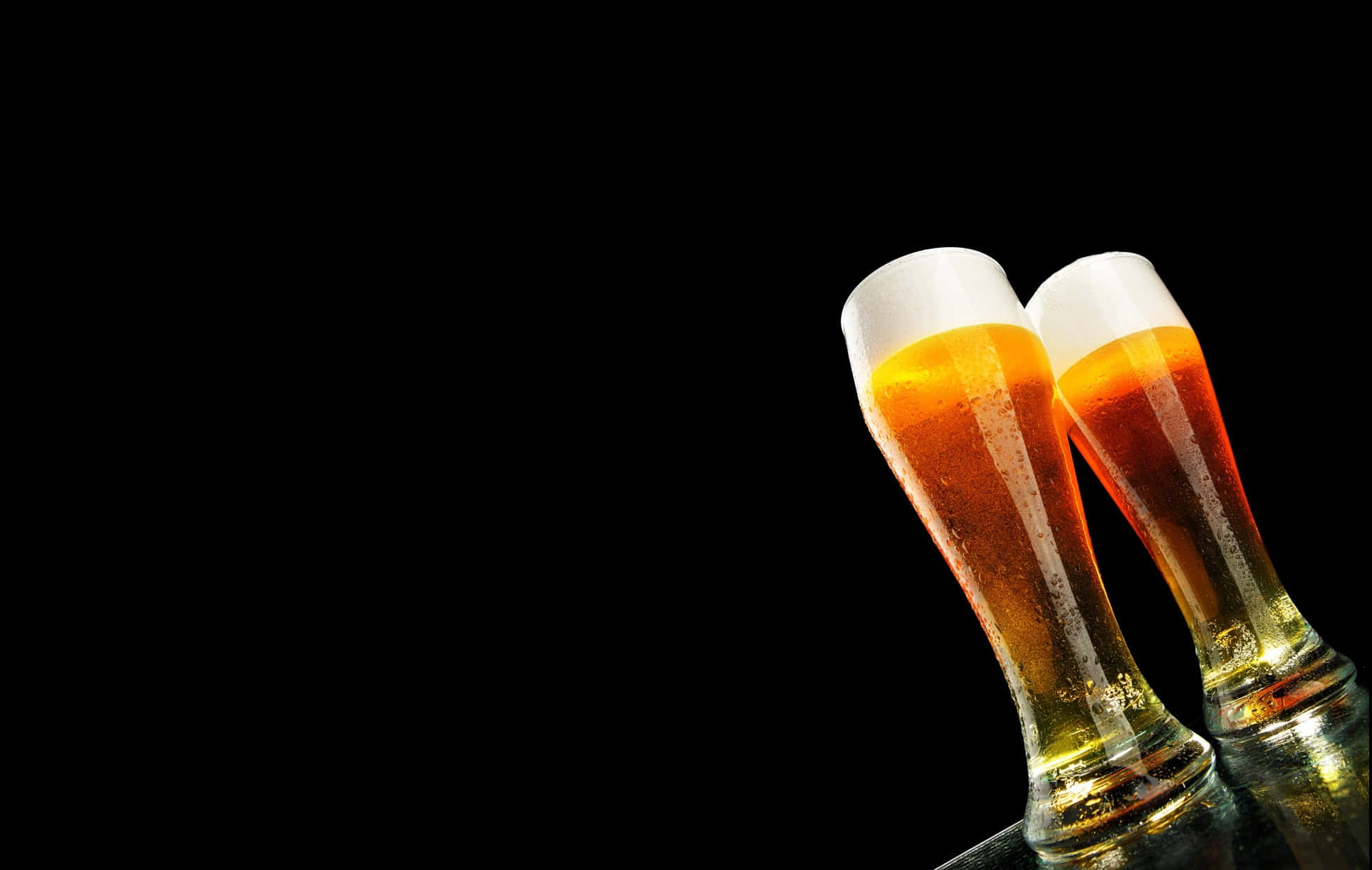 為美好的夜晚乾杯！ 壁紙 — 兩杯冰凍琥珀色啤酒杯帶有白色泡沫頭，在純黑背景上互相碰撞。