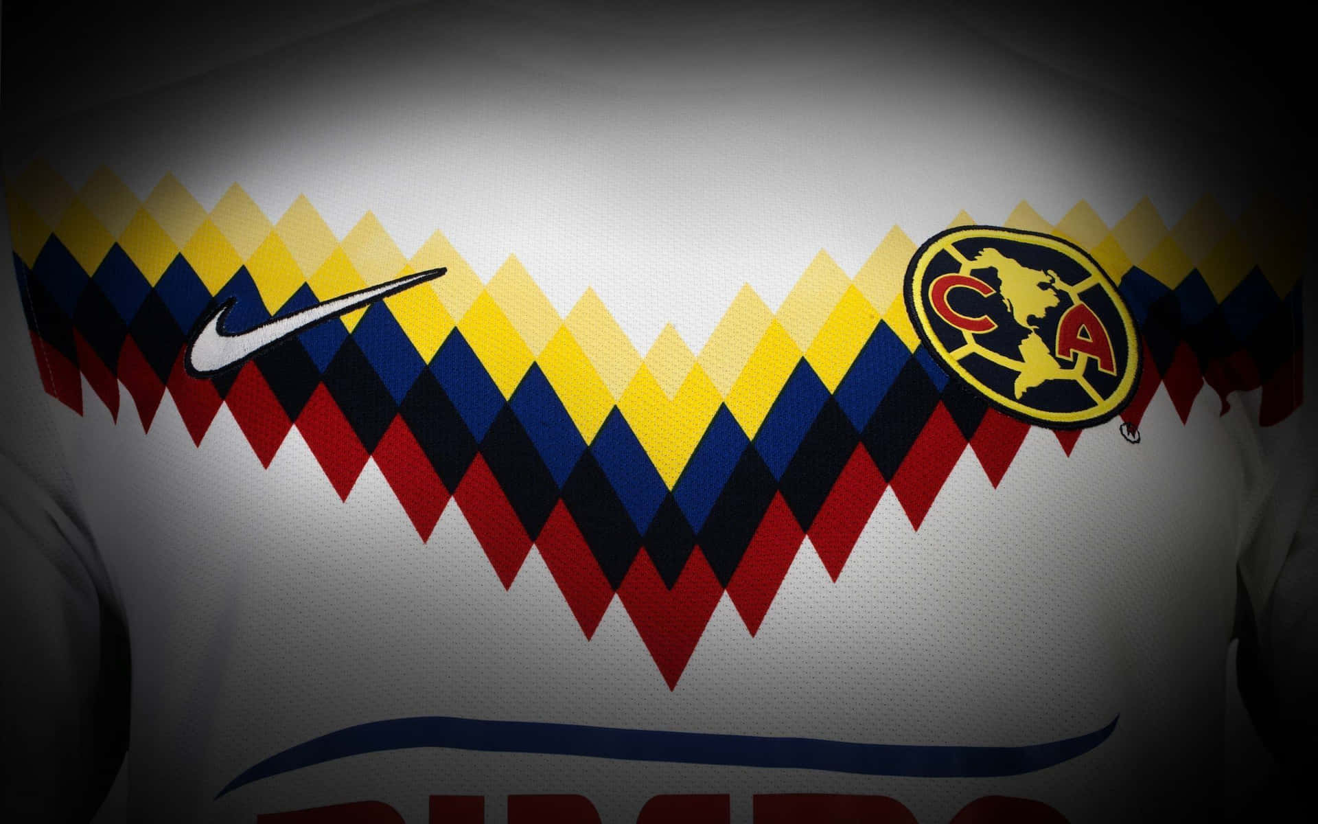白色足球球衣特寫，帶有紅、黃、藍色鋸齒圖案和 Club America 徽章。