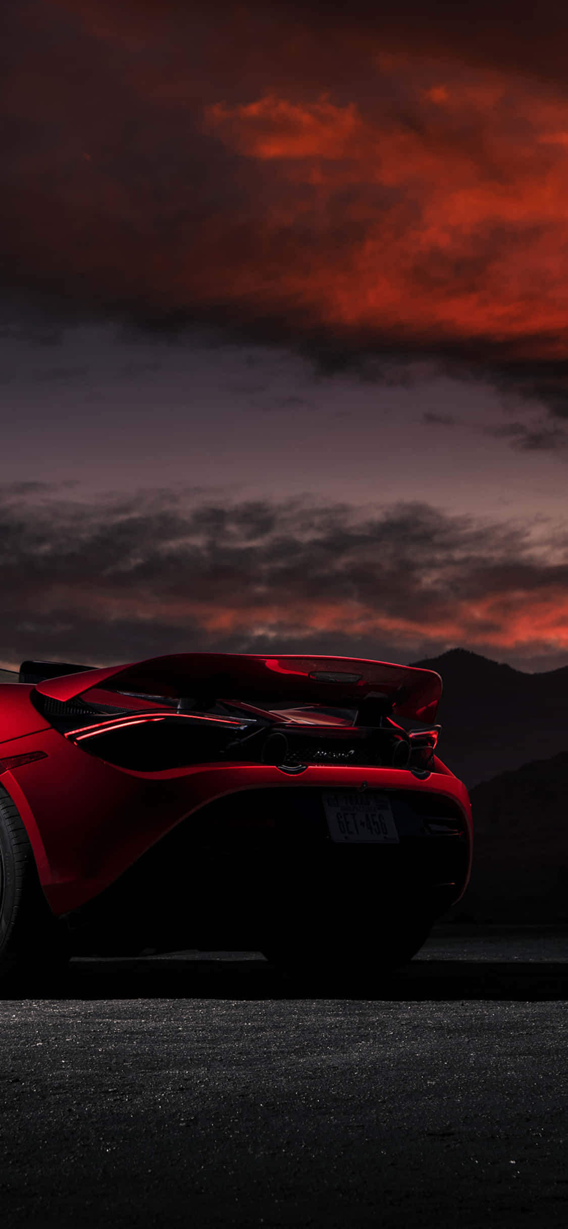 為速度與風格而生——iPhone Xs McLaren 720S 壁紙 — 一輛時尚的紅色跑車剪影在火熱的橙色和紫色日落天空下，映襯著遠山閃耀。