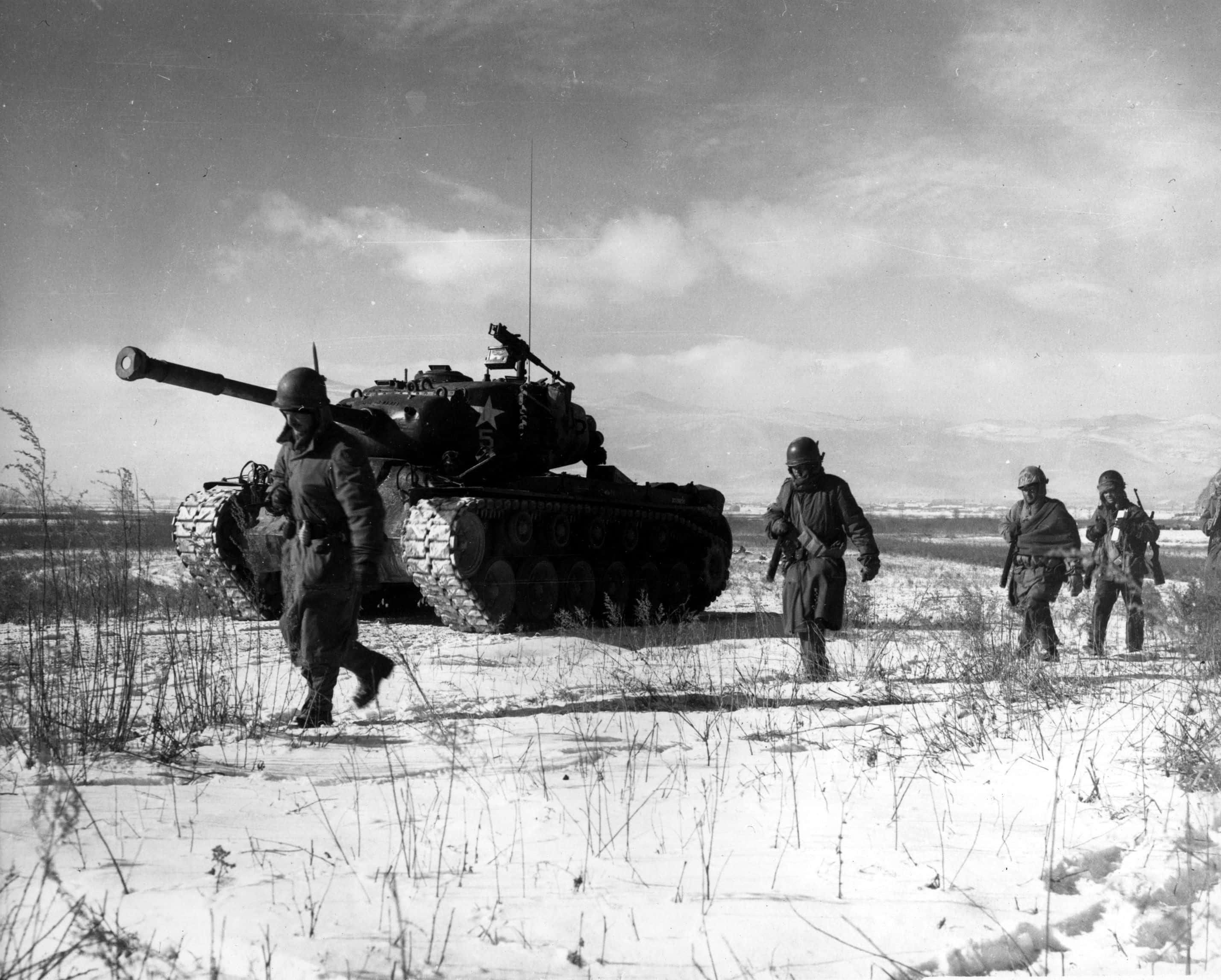 「烈火鍛造：戰爭的代價」 壁紙 — 士兵在多雲的天空下，穿過雪地，旁邊是一輛大型軍用坦克。
