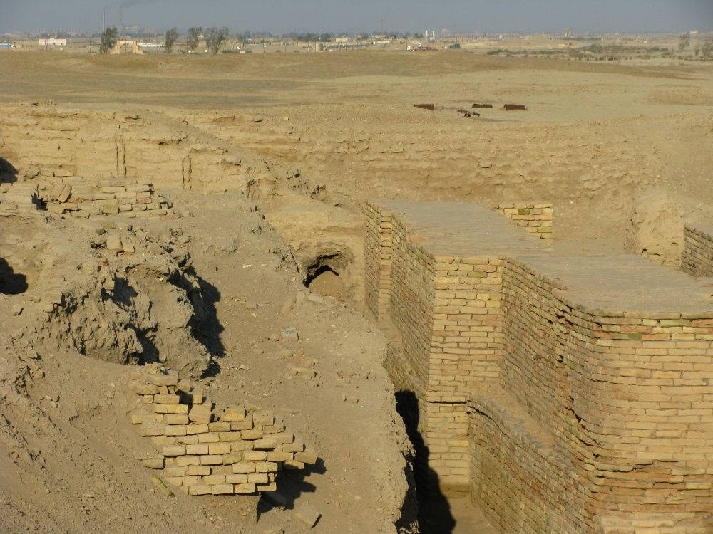 沙漠中的古老磚砌遺跡與遠處的現代建築。