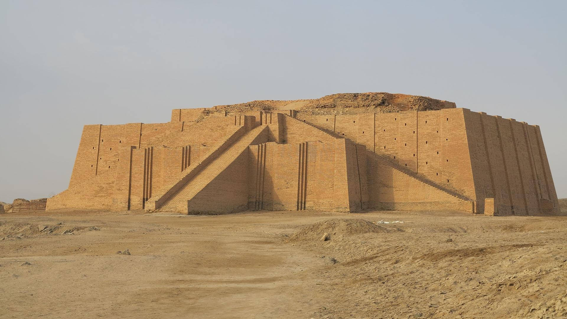 沙漠中的古代金字形神塔，陽光照射的磚層和沙質前景。