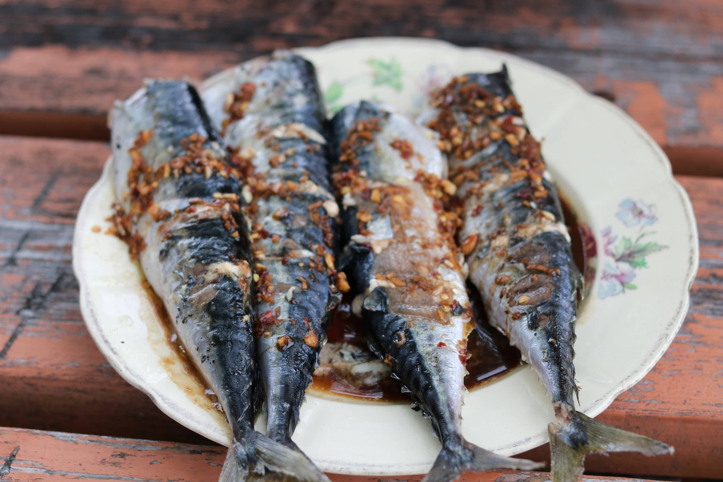 烤無頭鯡魚 壁紙 — 四塊烤鯖魚柳配上脆蒜和醬油，放在花紋碟上，置於經風化的木桌上。