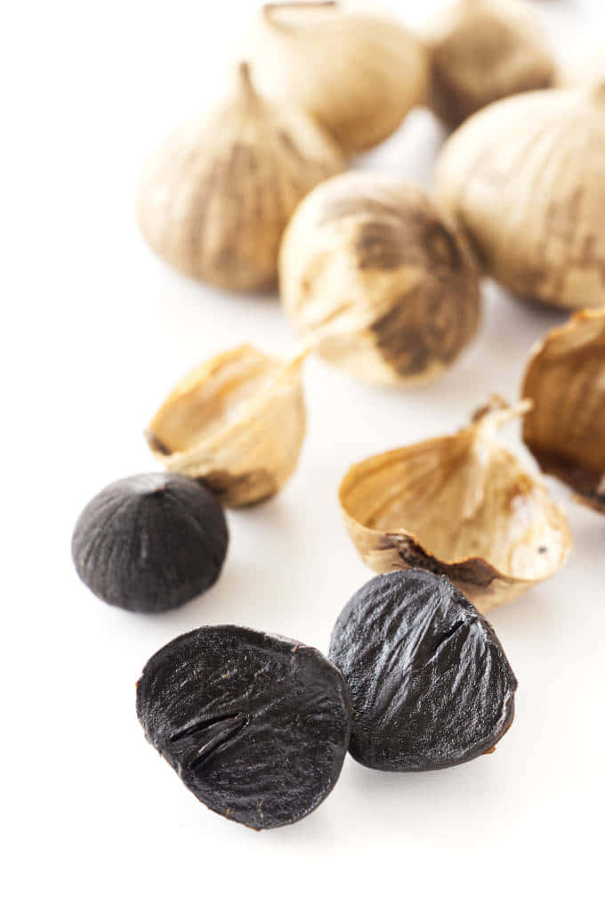 Black Garlic 桌布 壁紙 — 烤蒜頭和黑蒜瓣在亮白色表面上的特寫。