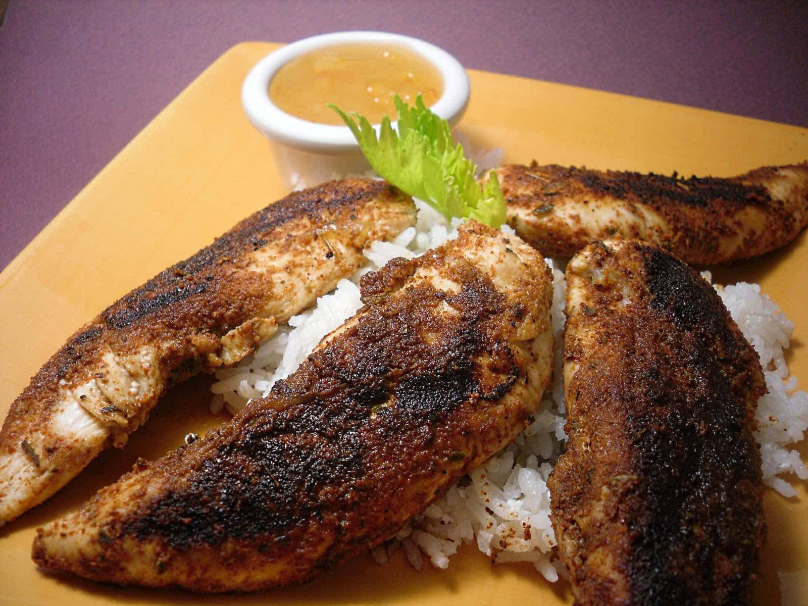 Blackened Chicken 桌布 壁紙 — 烤雞胸肉配焦香香料，放在白飯上，置於黃色碟中，伴以蘸醬和新鮮生菜。