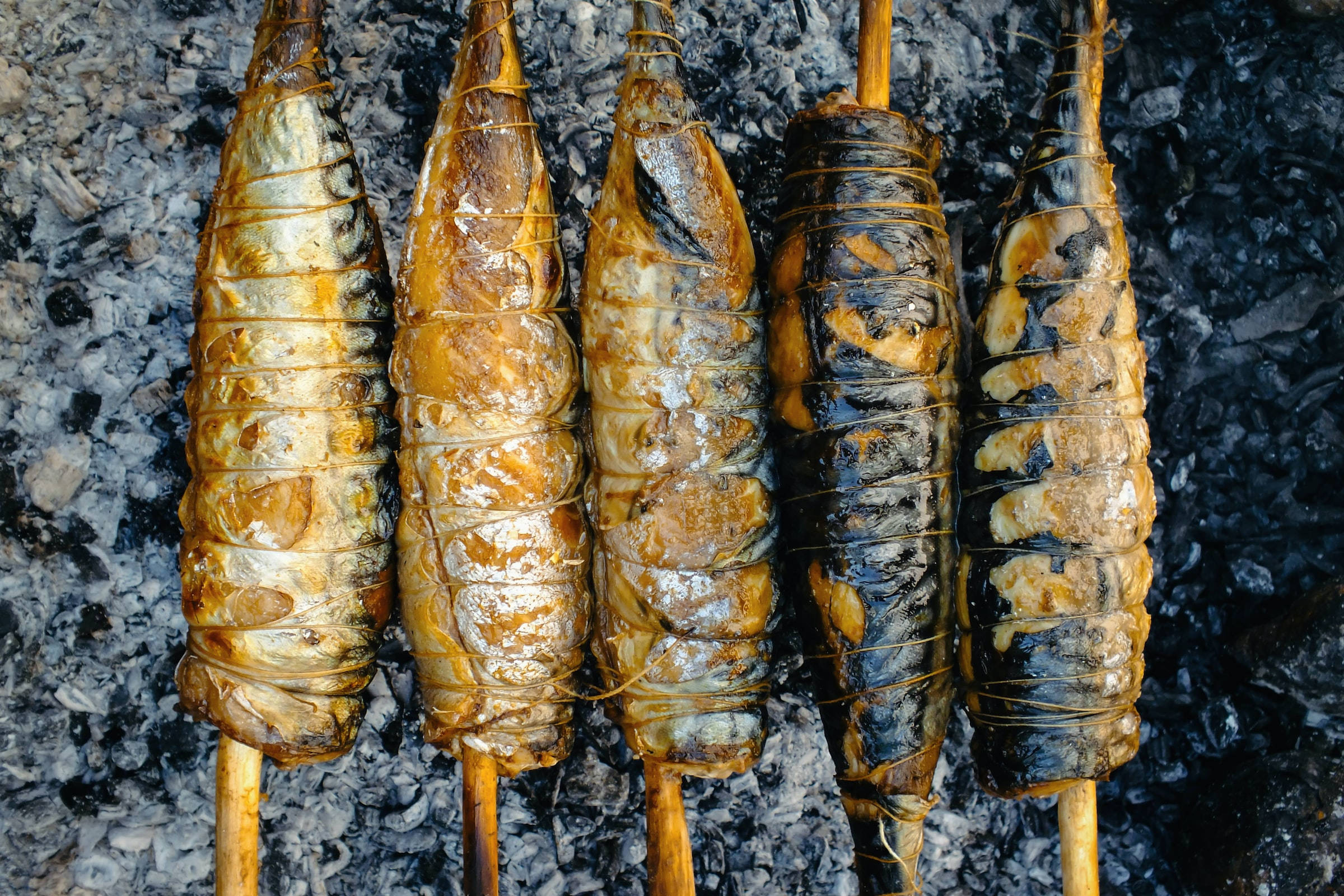 烤鰹魚：海鮮愛好者的盛宴 壁紙 — 五條整魚用繩子捆綁，在熾熱的炭火上燒烤，魚皮焦黑，外皮金黃酥脆。