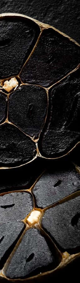 Black Garlic 桌布 壁紙 — 烤黑蒜瓣的特寫，展現出光澤的深色外皮和金棕色的內膜。