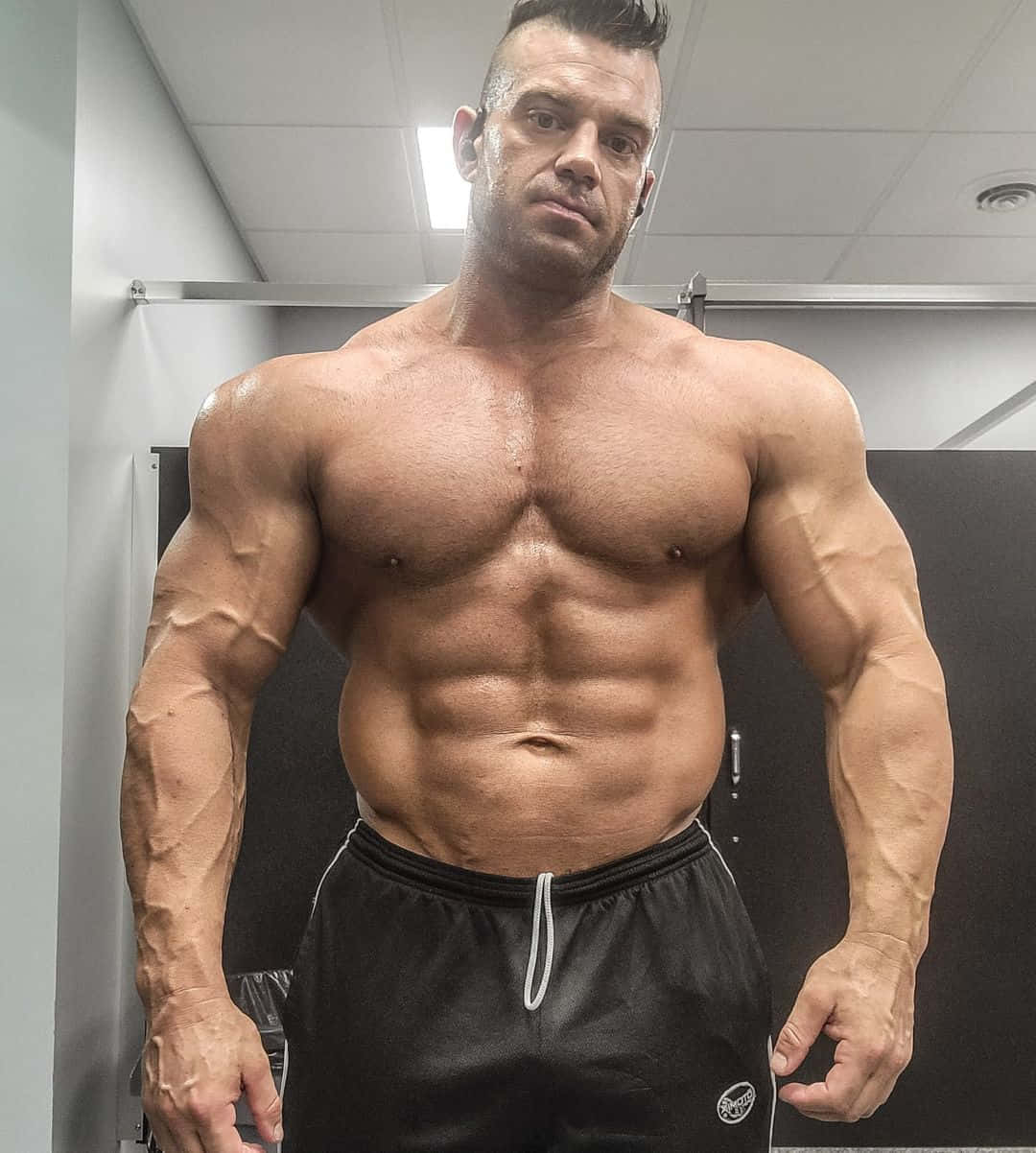 一個肌肉男在健身室更衣室展示手臂和腹肌。