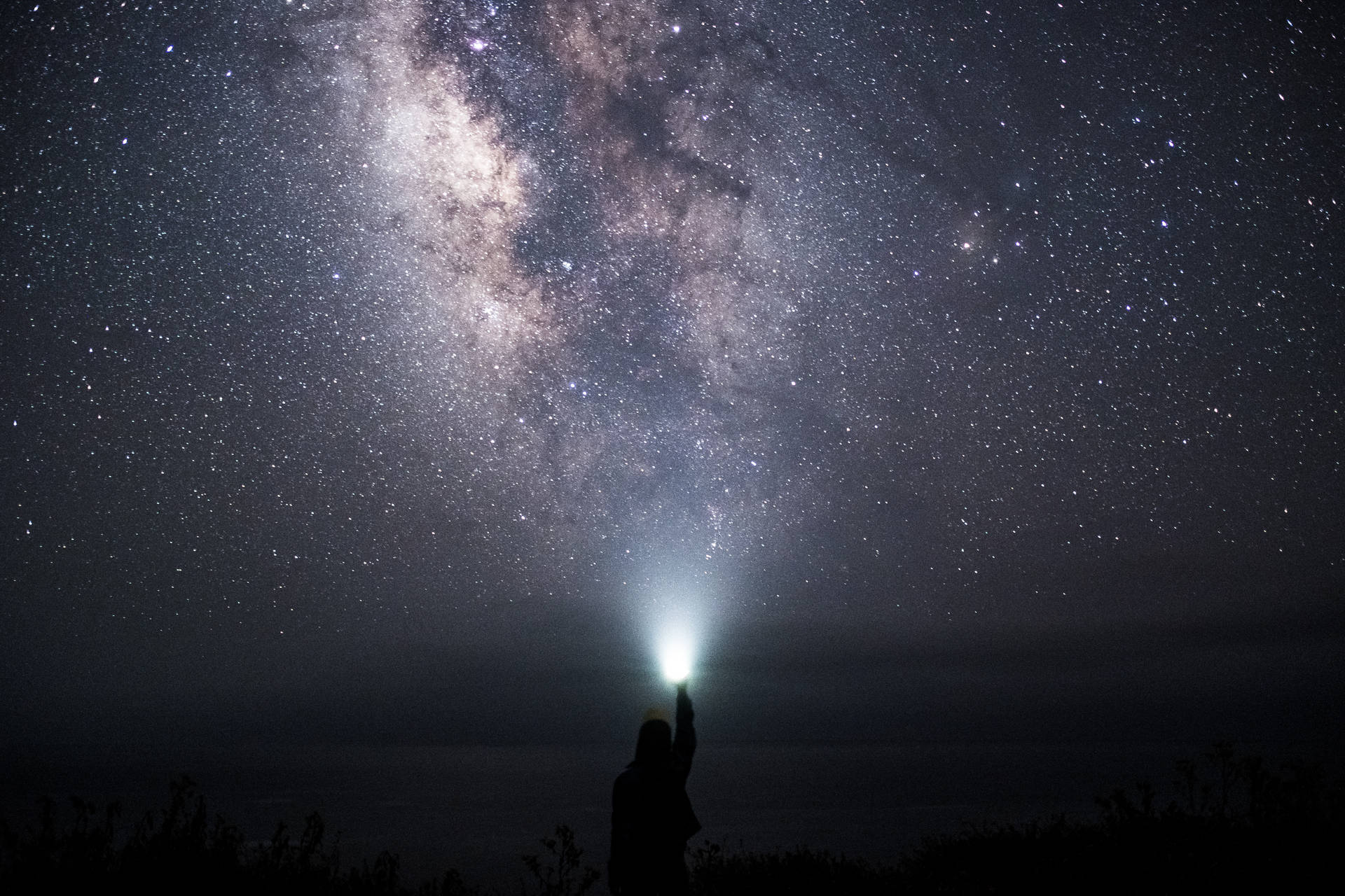 人將手電筒指向天空，顯現銀河星辰